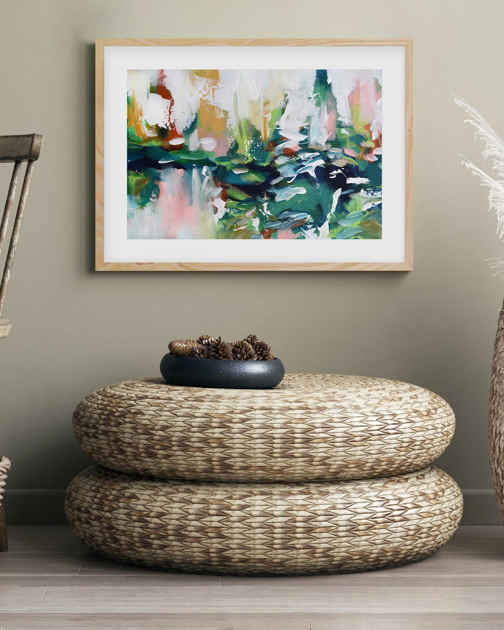 Woven ottoman with a decorative bowl on a wooden floor, framed abstract art on the wall.