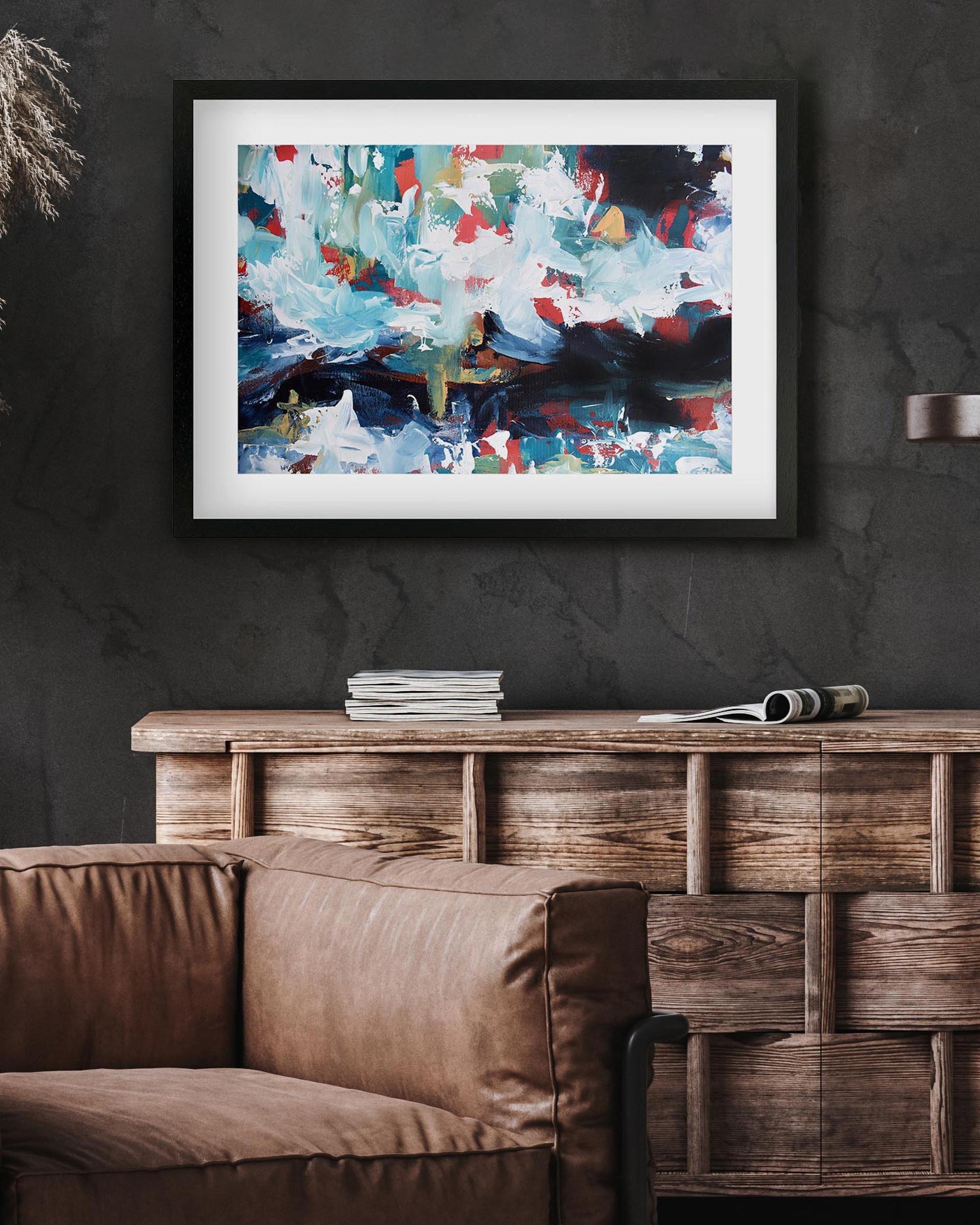 Framed abstract painting on a dark wall above a wooden console table with books and a newspaper.