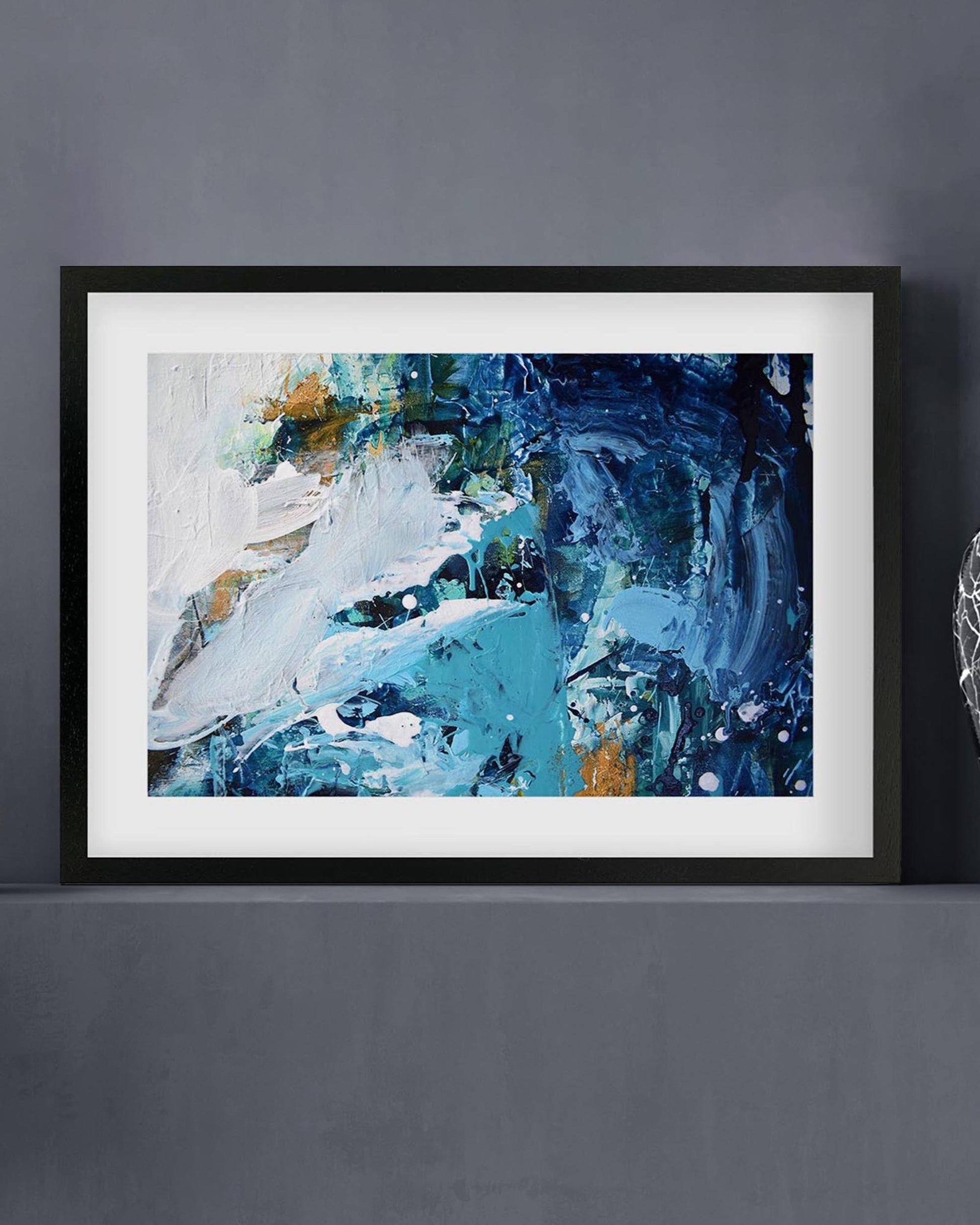 Framed abstract art piece with blue and white tones on a gray wall