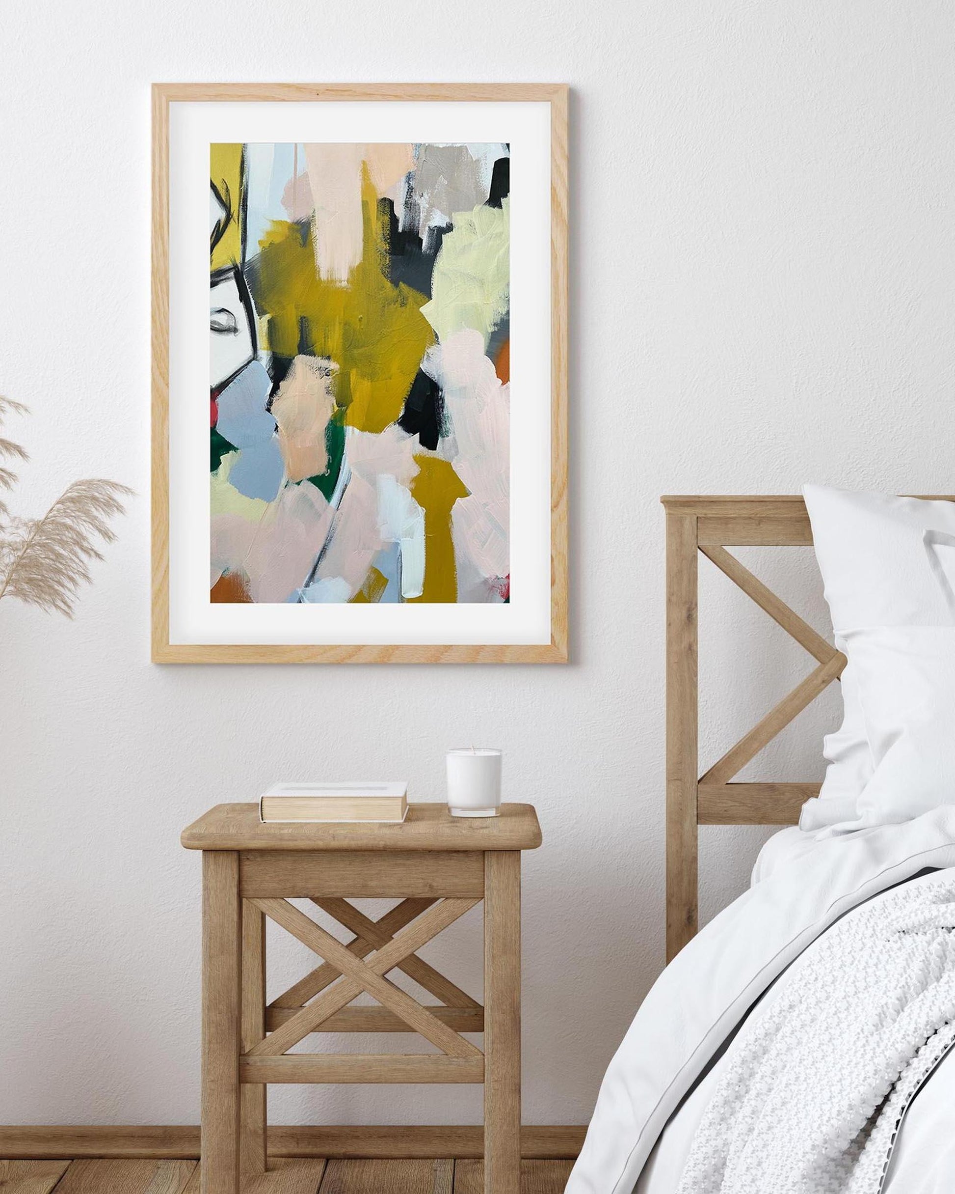 Abstract art print in a wooden frame on a wall above a wooden side table.