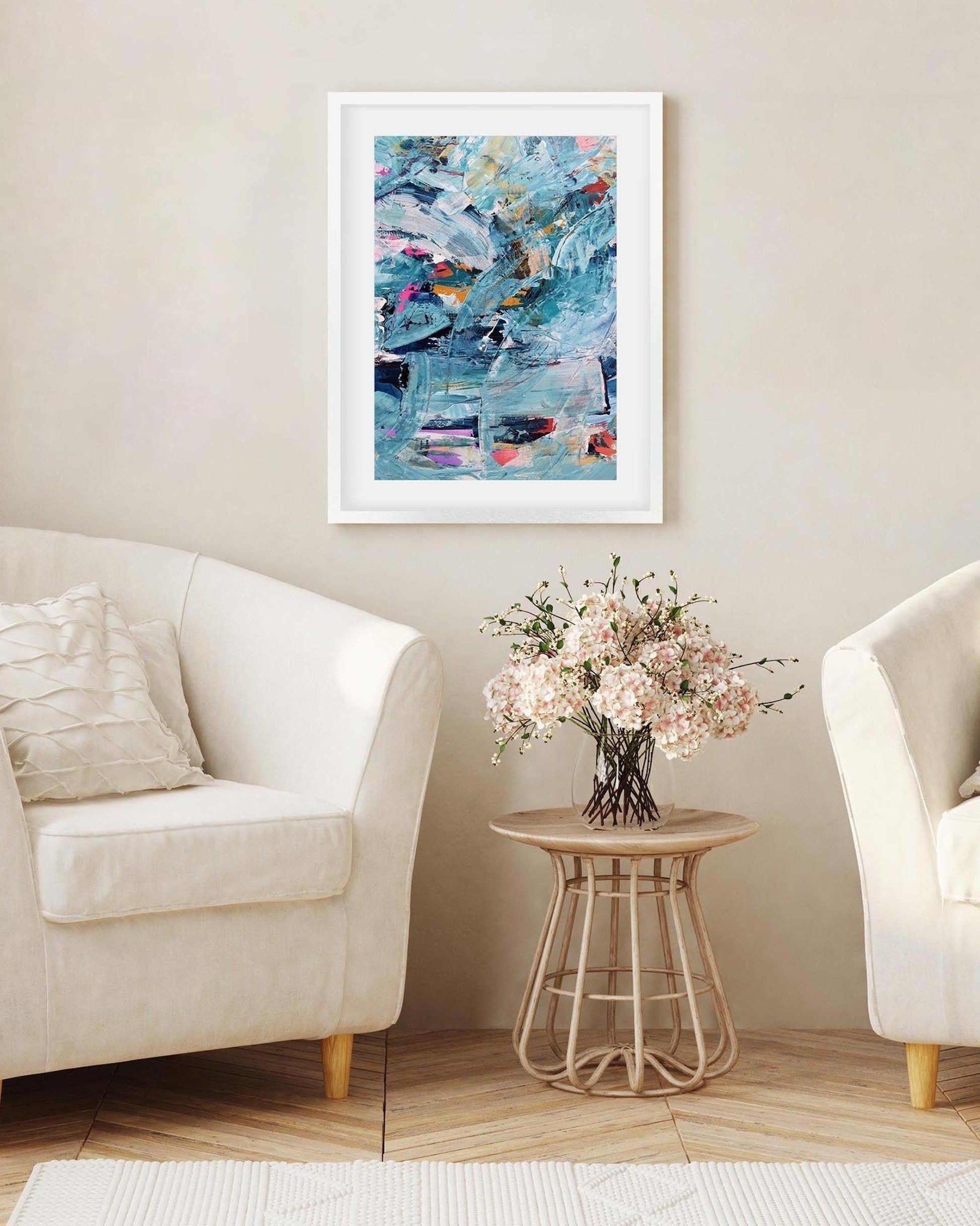 Framed abstract painting on a wall above a side table with flowers in a living room.
