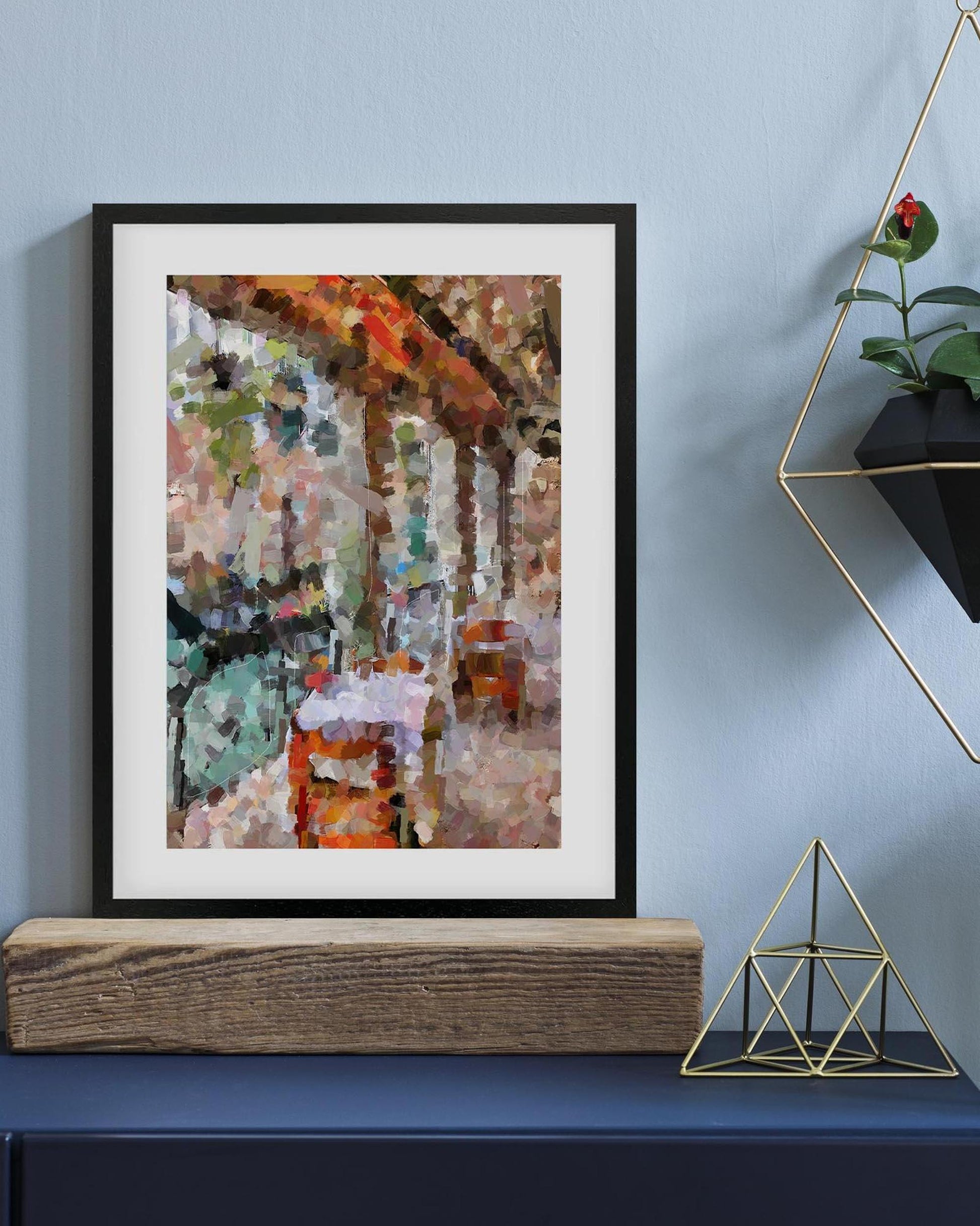 Framed abstract artwork on a shelf with decorative elements against a blue wall