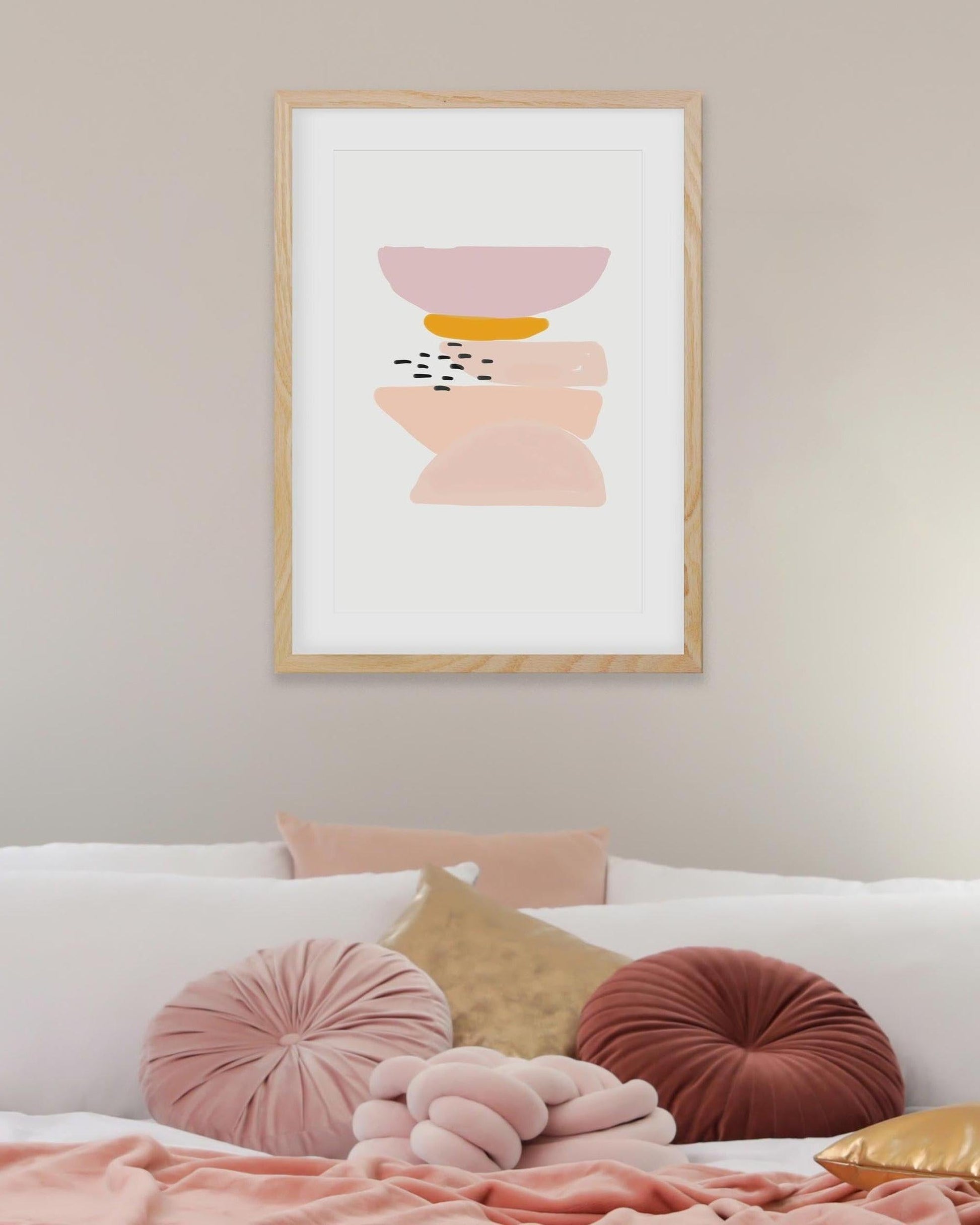 Framed abstract art print on a wall above a bed with colorful pillows.