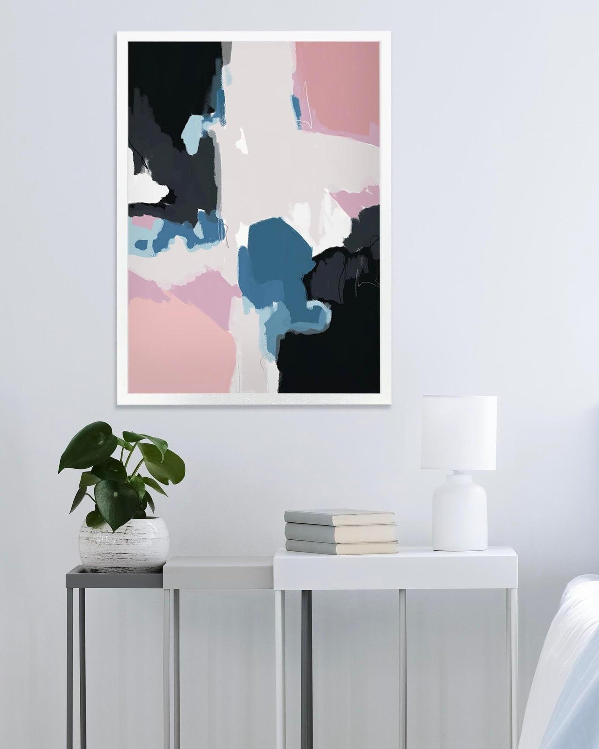 Abstract art print on a wall above a side table with a plant and books.