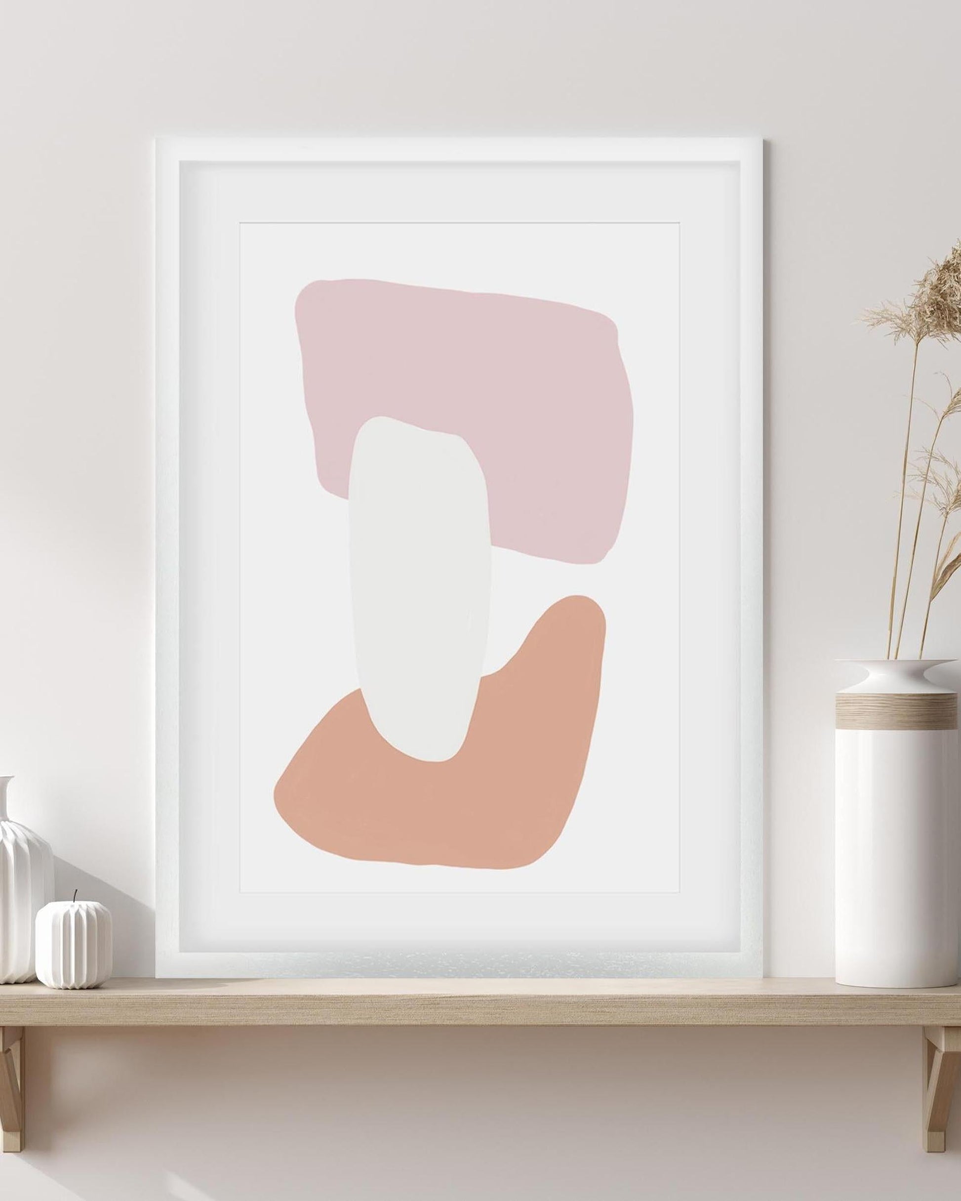 Abstract art print with pink and white shapes in a white frame on a wall.