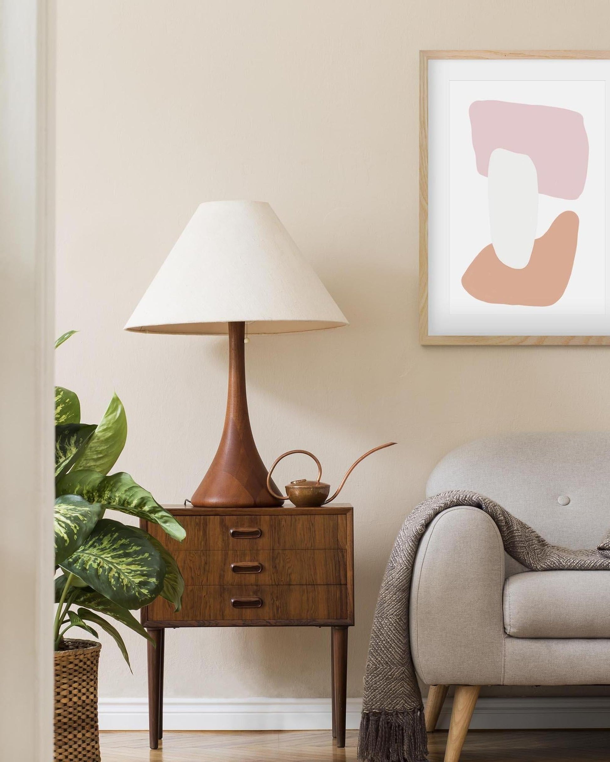 Nest living room with a lamp on a wooden side table, plant, and abstract art on the wall.