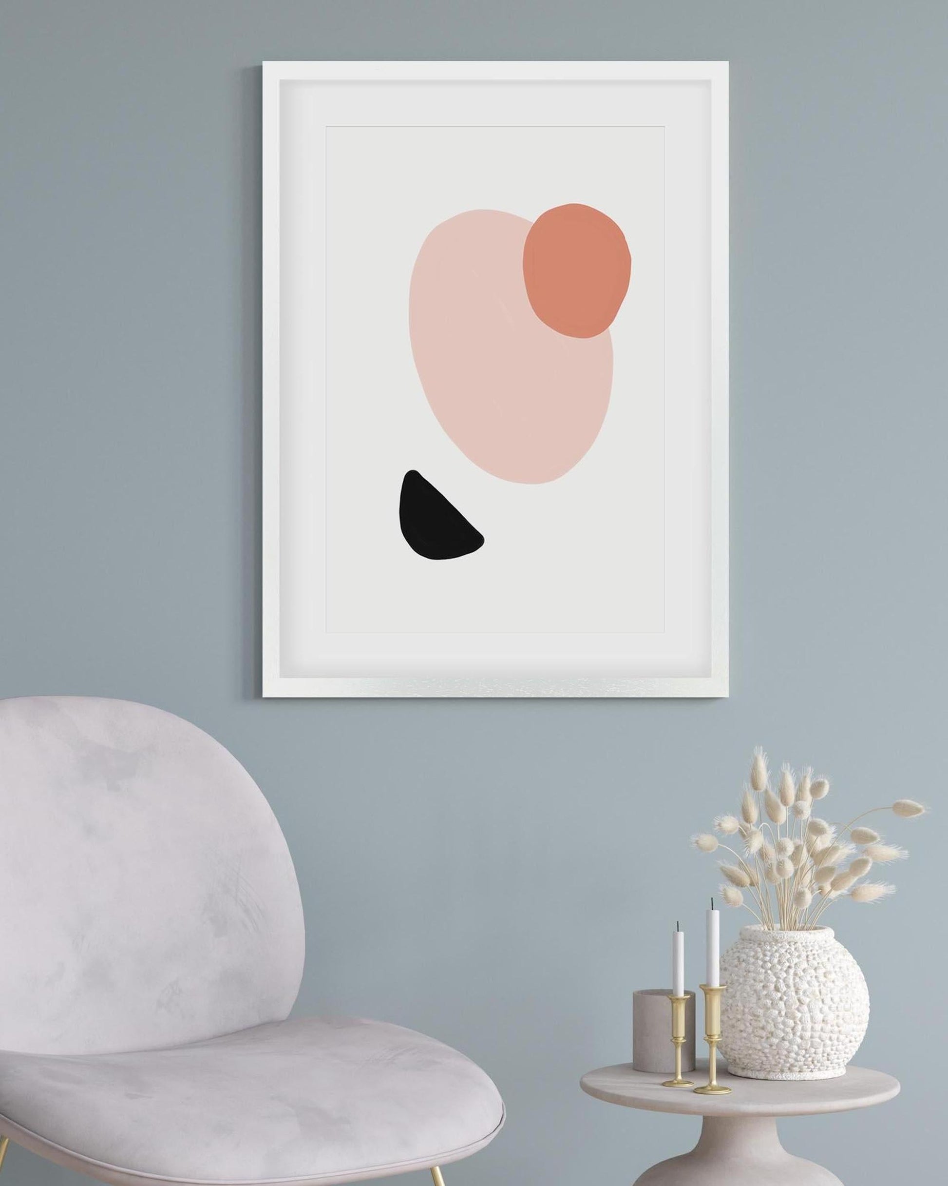 Framed abstract art print with pink, black, and red shapes on a light blue wall.