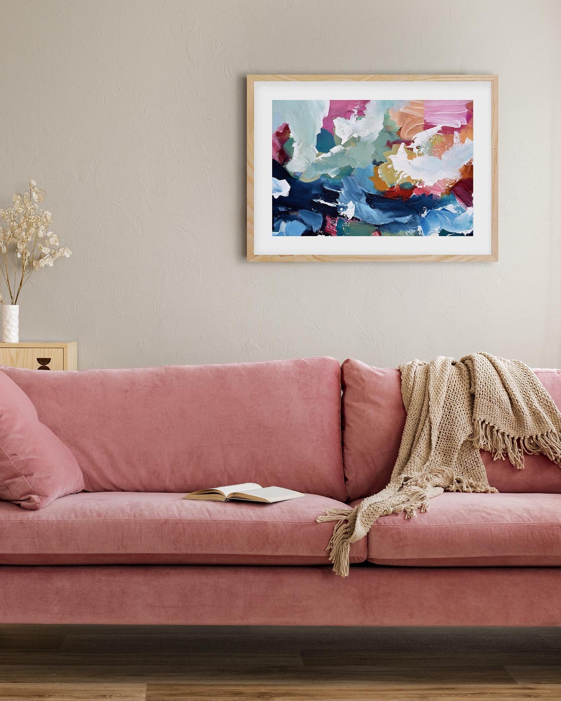 Pink sofa in a living room with a colorful abstract painting on the wall.
