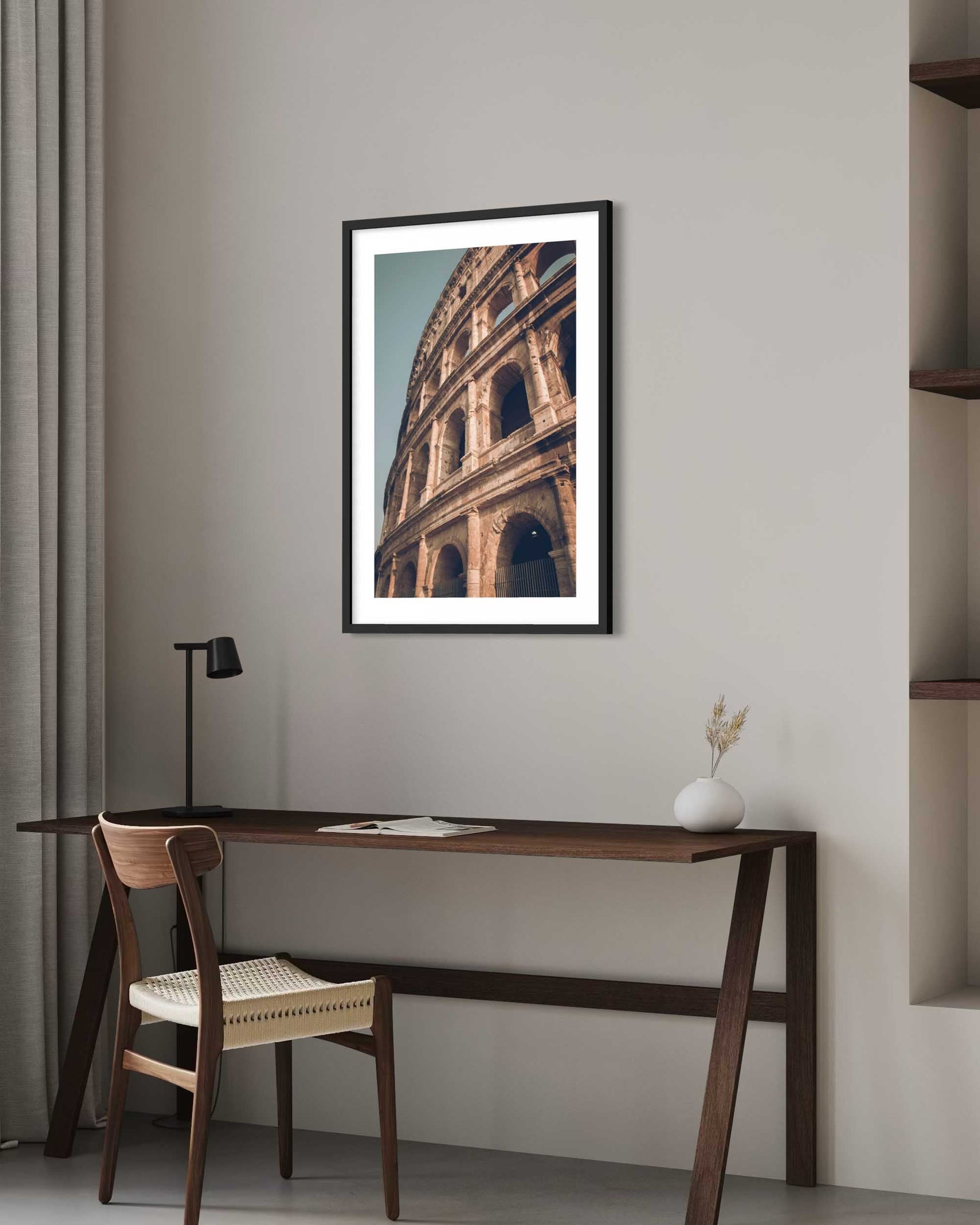 Framed artwork of a architectural structure on a wall above a desk and chair.