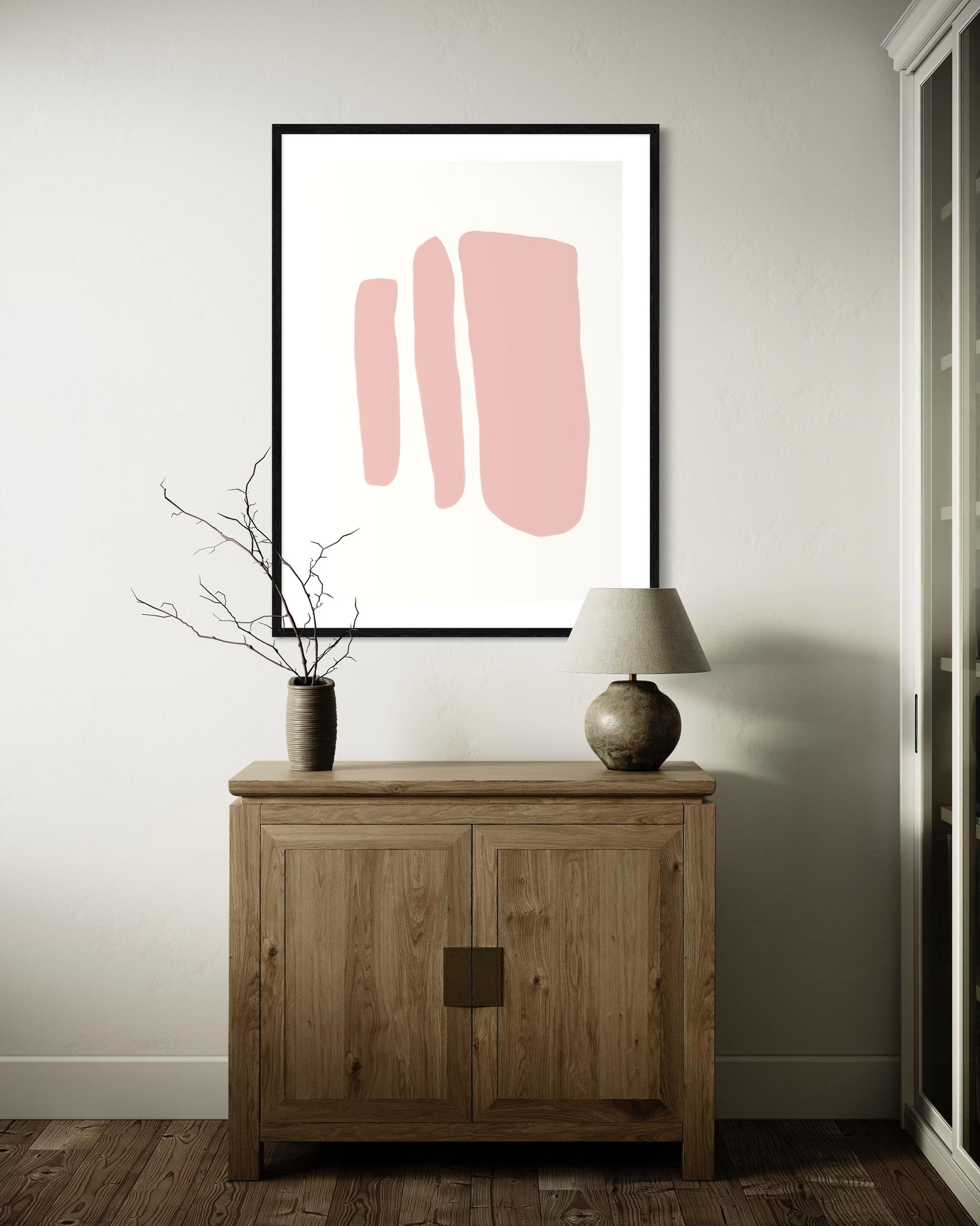 Framed abstract art with pink shapes on a wall above a wooden cabinet.