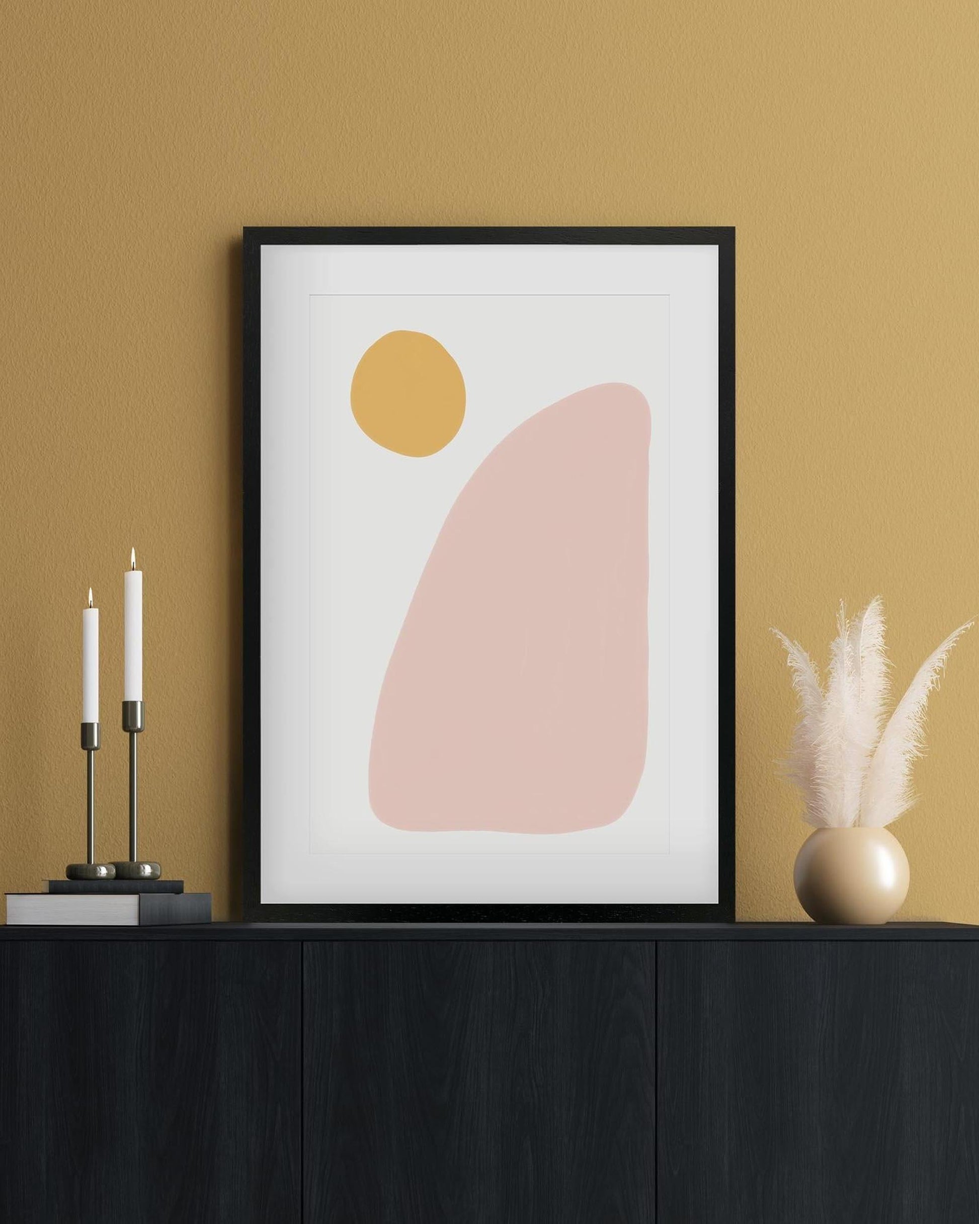 Framed abstract art print with a yellow circle and pink shape on a beige wall.
