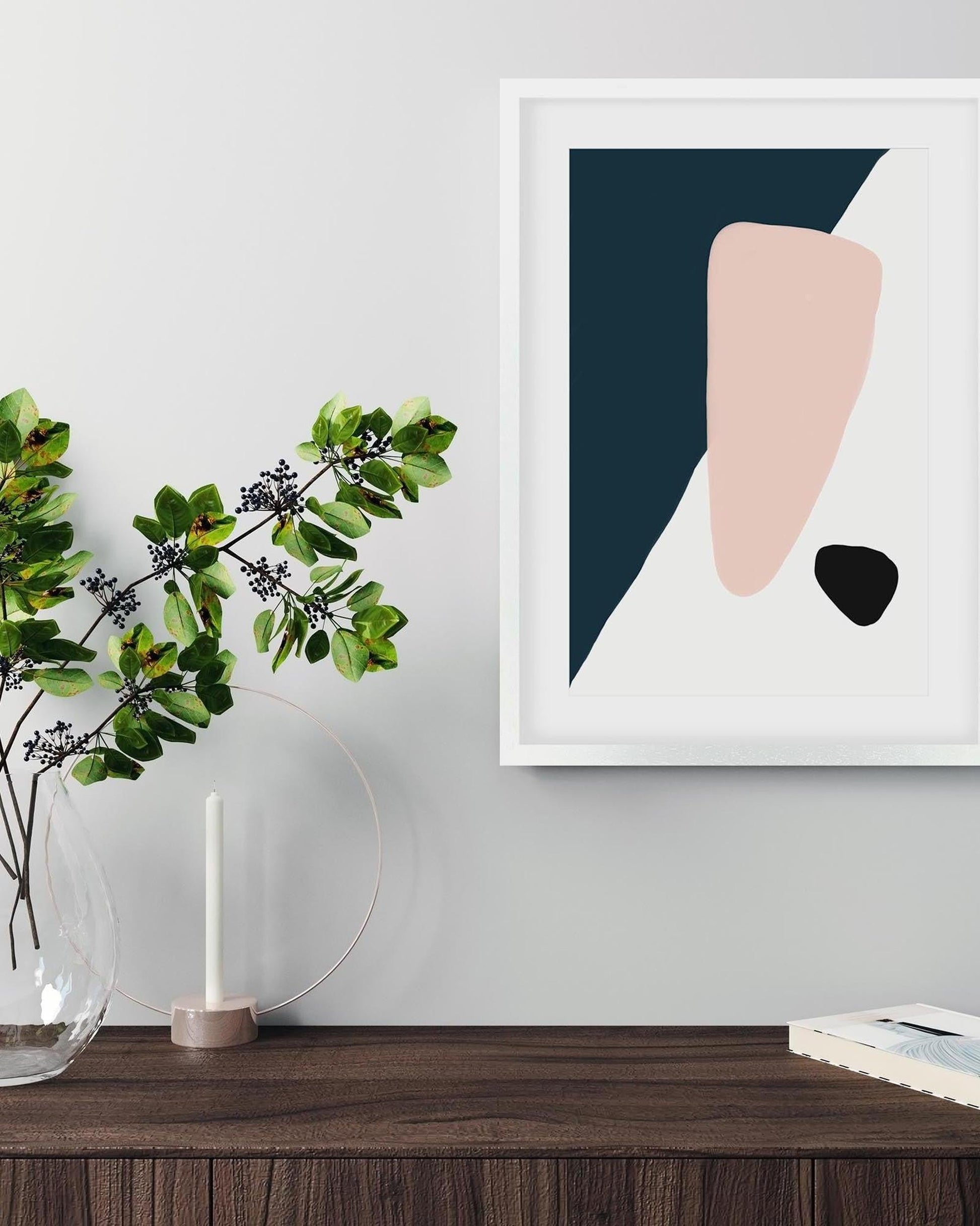 Abstract art print with geometric shapes on a wall above a wooden surface with a plant and candle.