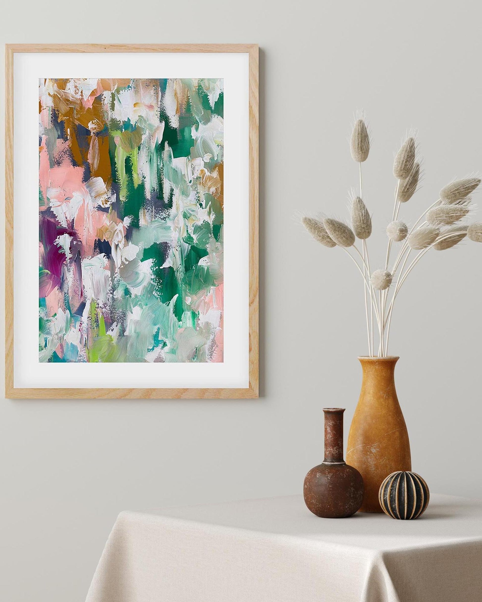 Framed abstract art on a wall with decorative vases and plants on a table.