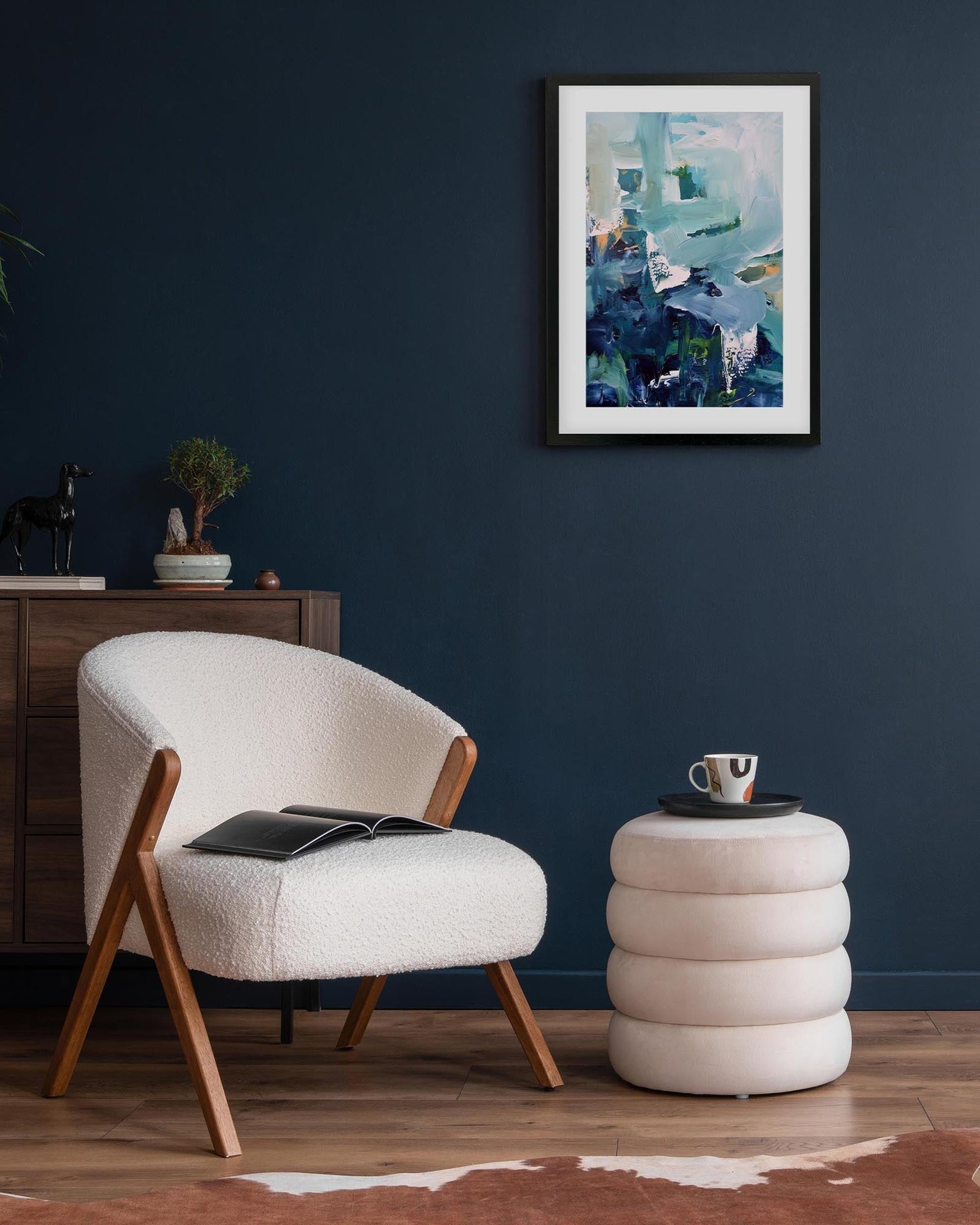 Modern living room with a white armchair, side table, and abstract artwork on a dark blue wall.