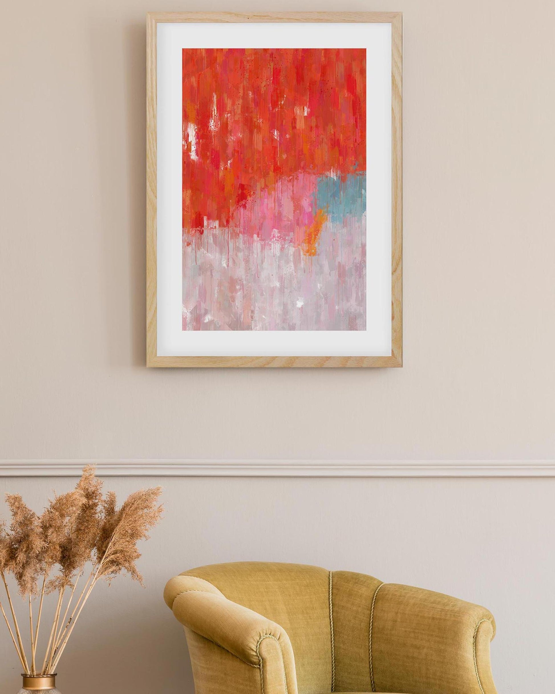 Abstract painting in a wooden frame on a beige wall above a yellow armchair.