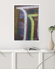 Framed abstract art piece on a white wall above a white cabinet with an open book and a vase.