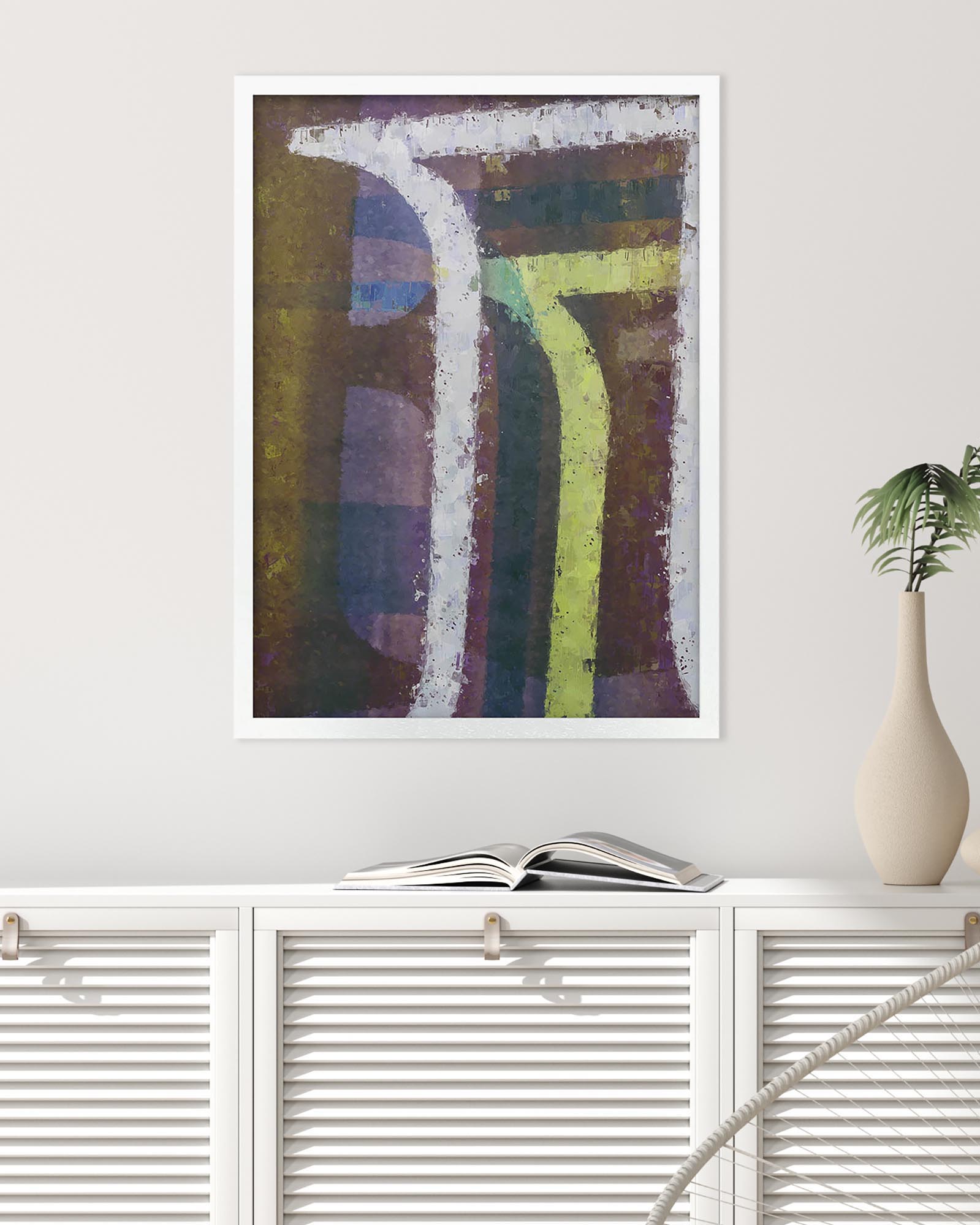 Framed abstract art piece on a white wall above a white cabinet with an open book and a vase.