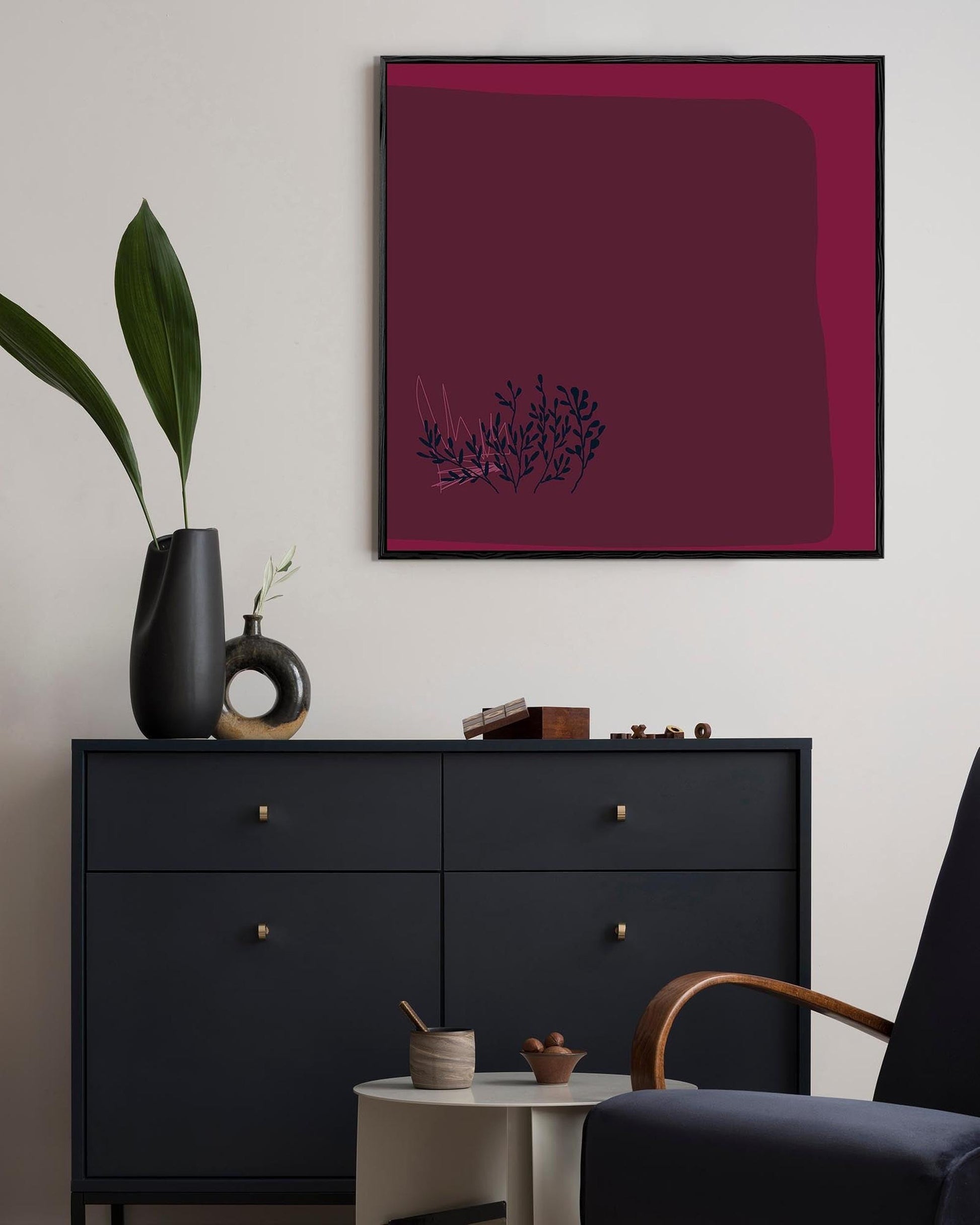 Modern interior with a black dresser, plant, and abstract art on a white wall.