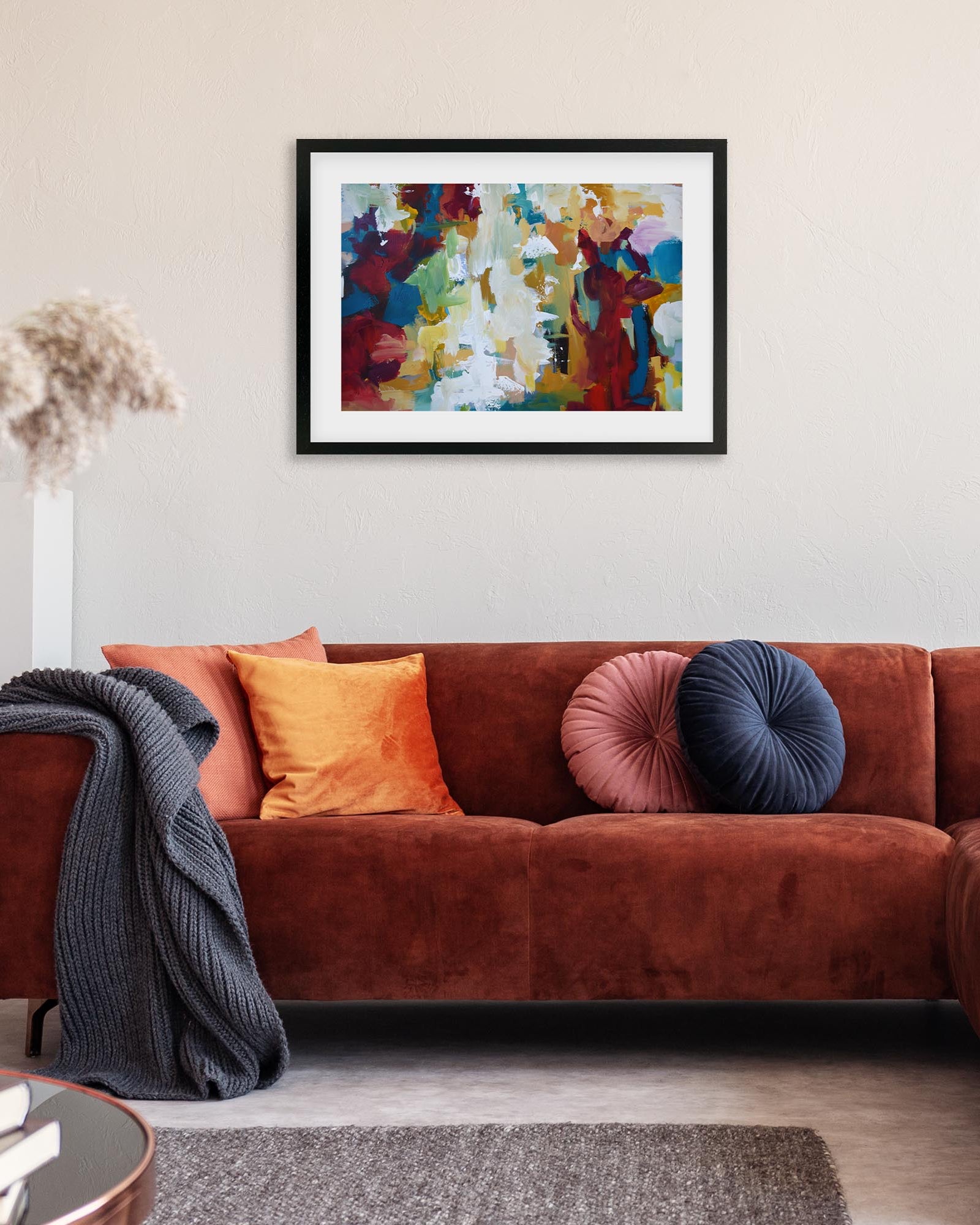 Living room with a brown sofa, colorful pillows, and a framed abstract painting on the wall.