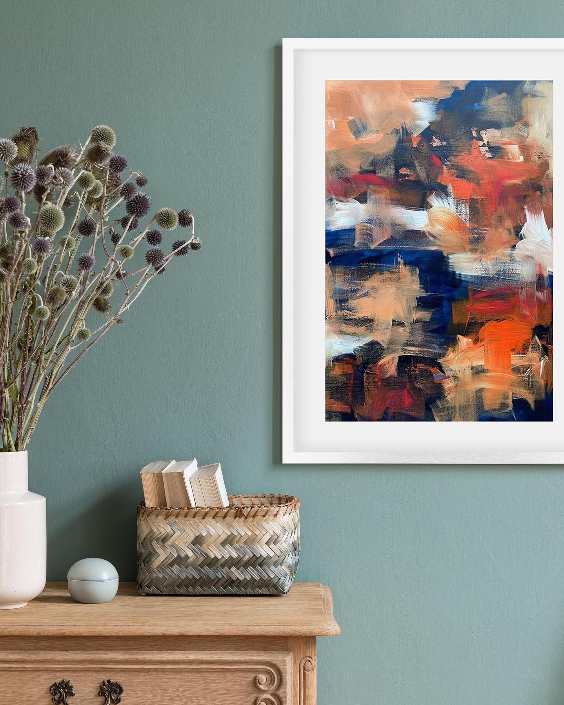 Abstract painting on a wall with a vase, basket, and small ball on a wooden surface below.