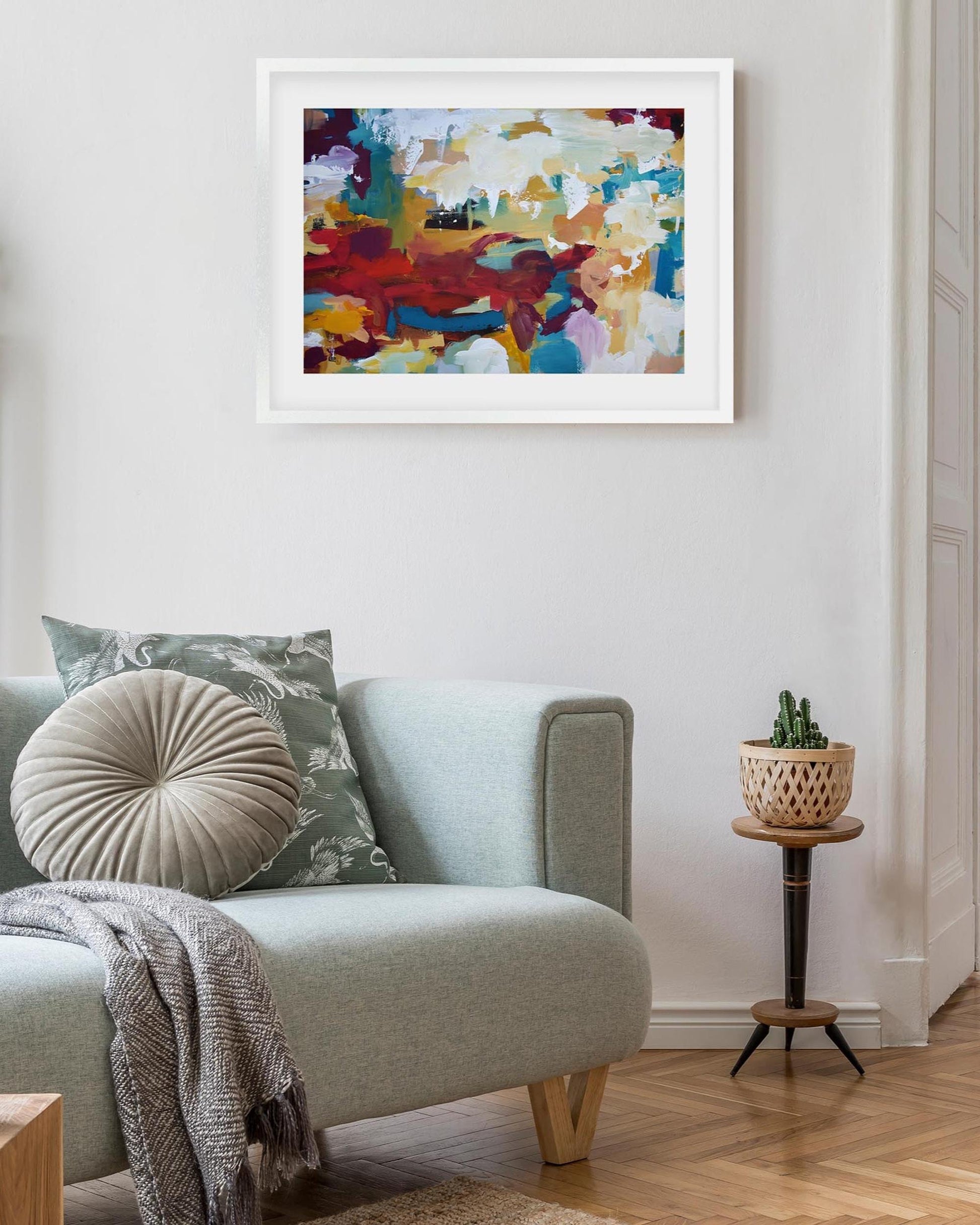 Living room with a gray sofa, colorful abstract painting, and small table with a plant.