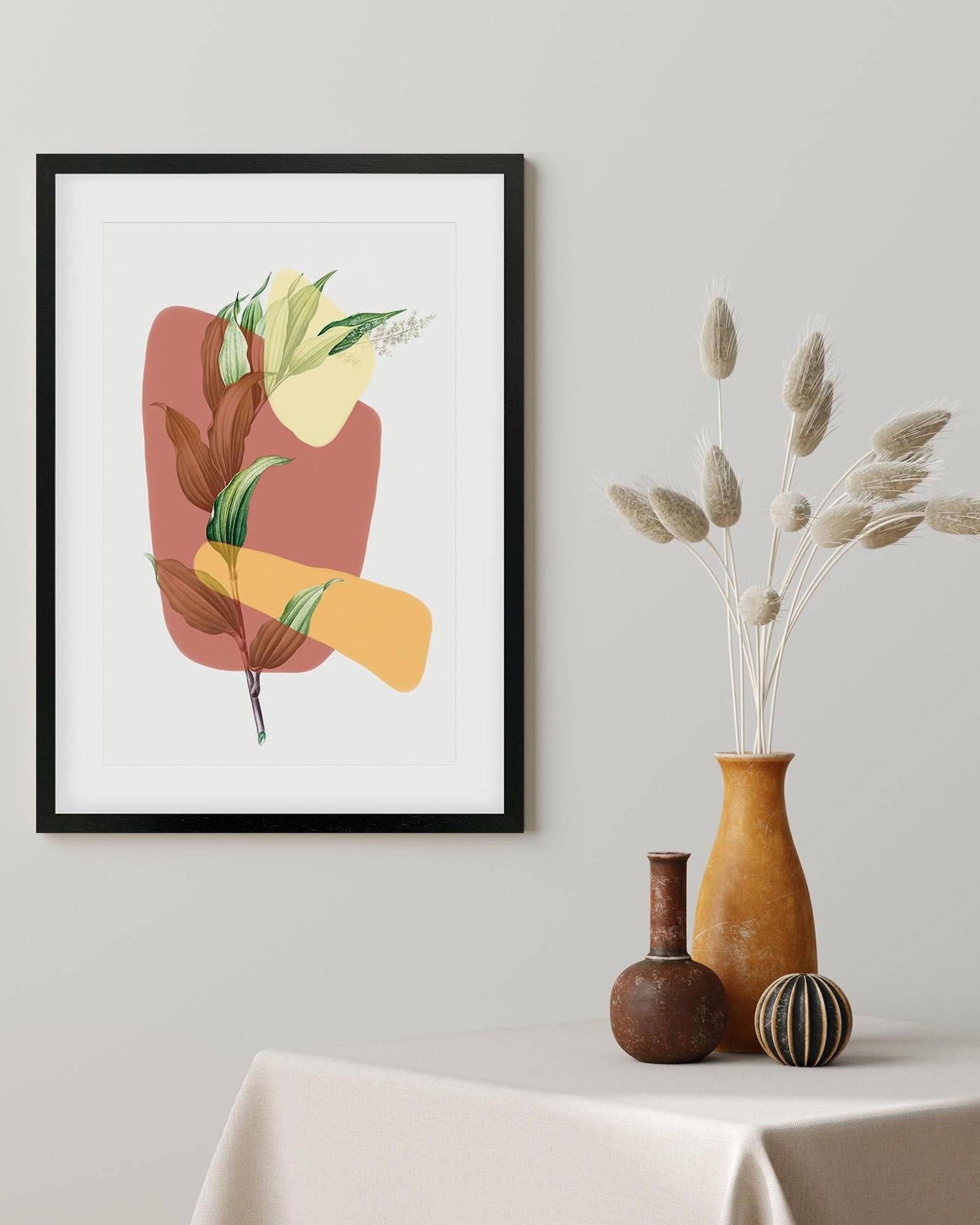 Framed abstract art print with leaves on a wall above a table with decorative vases.