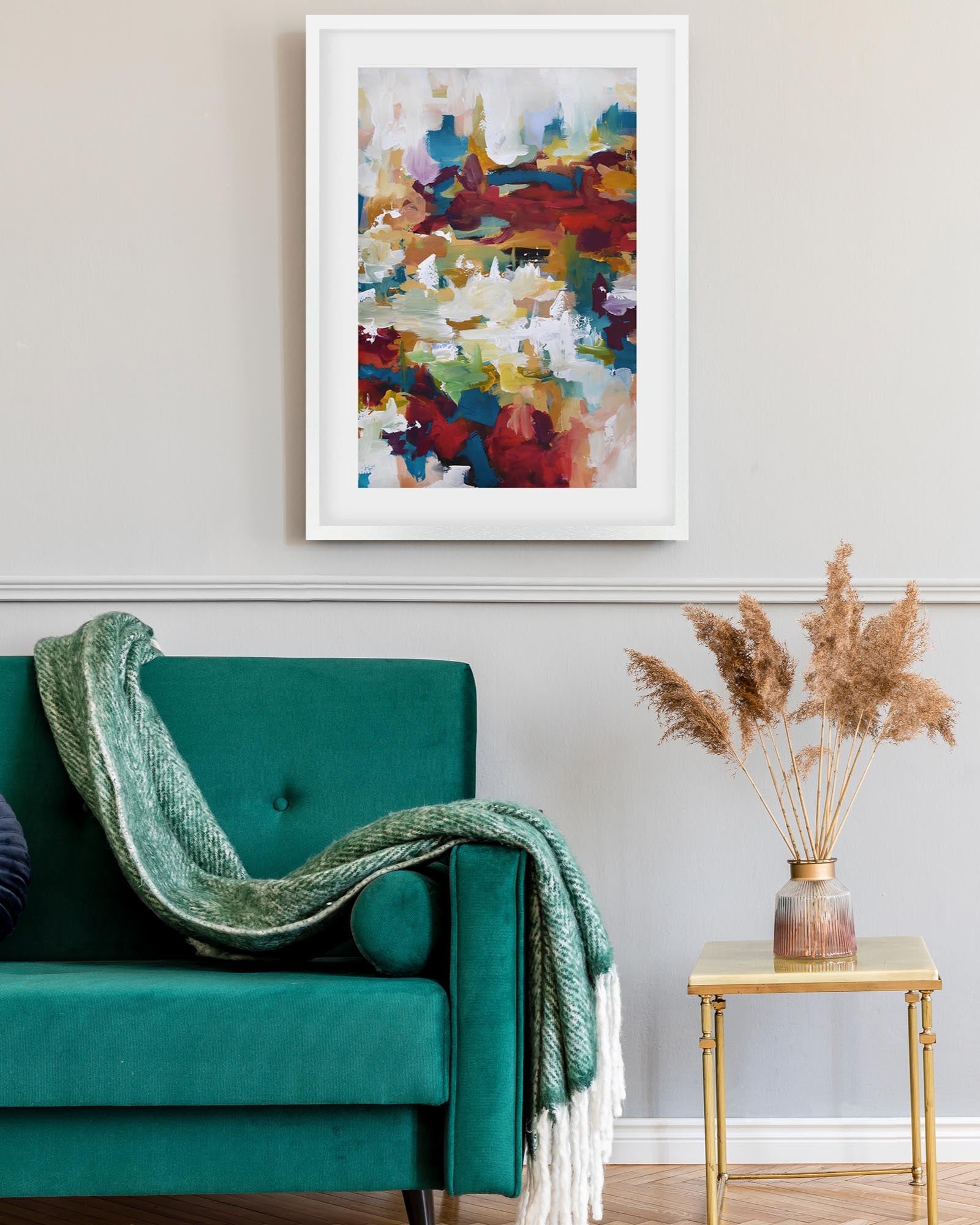 Colorful abstract painting on a wall above a teal sofa with a green blanket.