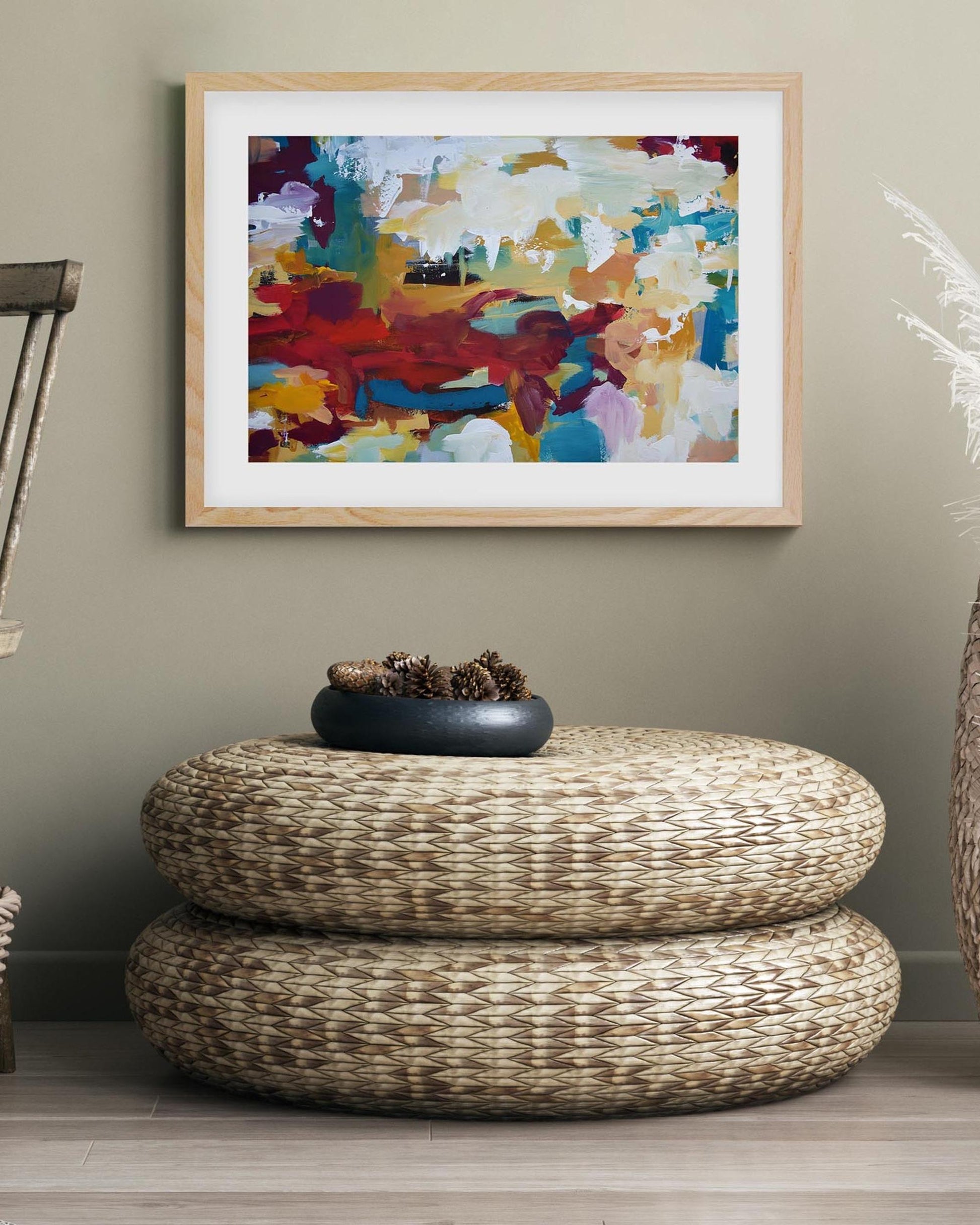 Woven ottoman with a decorative bowl, framed abstract art on the wall, and a wooden chair.