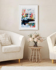Living room with two white armchairs, a small table with flowers, and a colorful abstract painting on the wall.