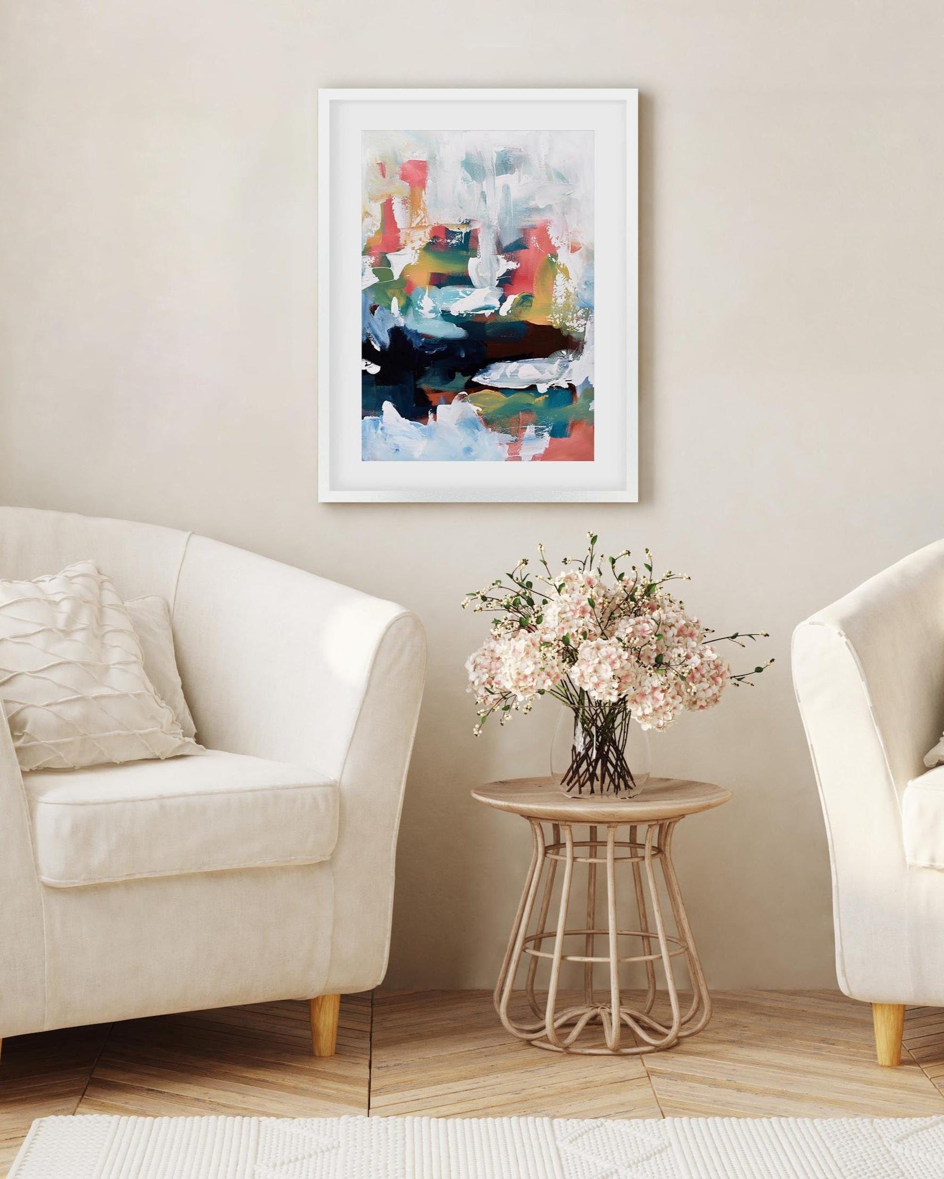 Living room with two white armchairs, a small table with flowers, and a colorful abstract painting on the wall.