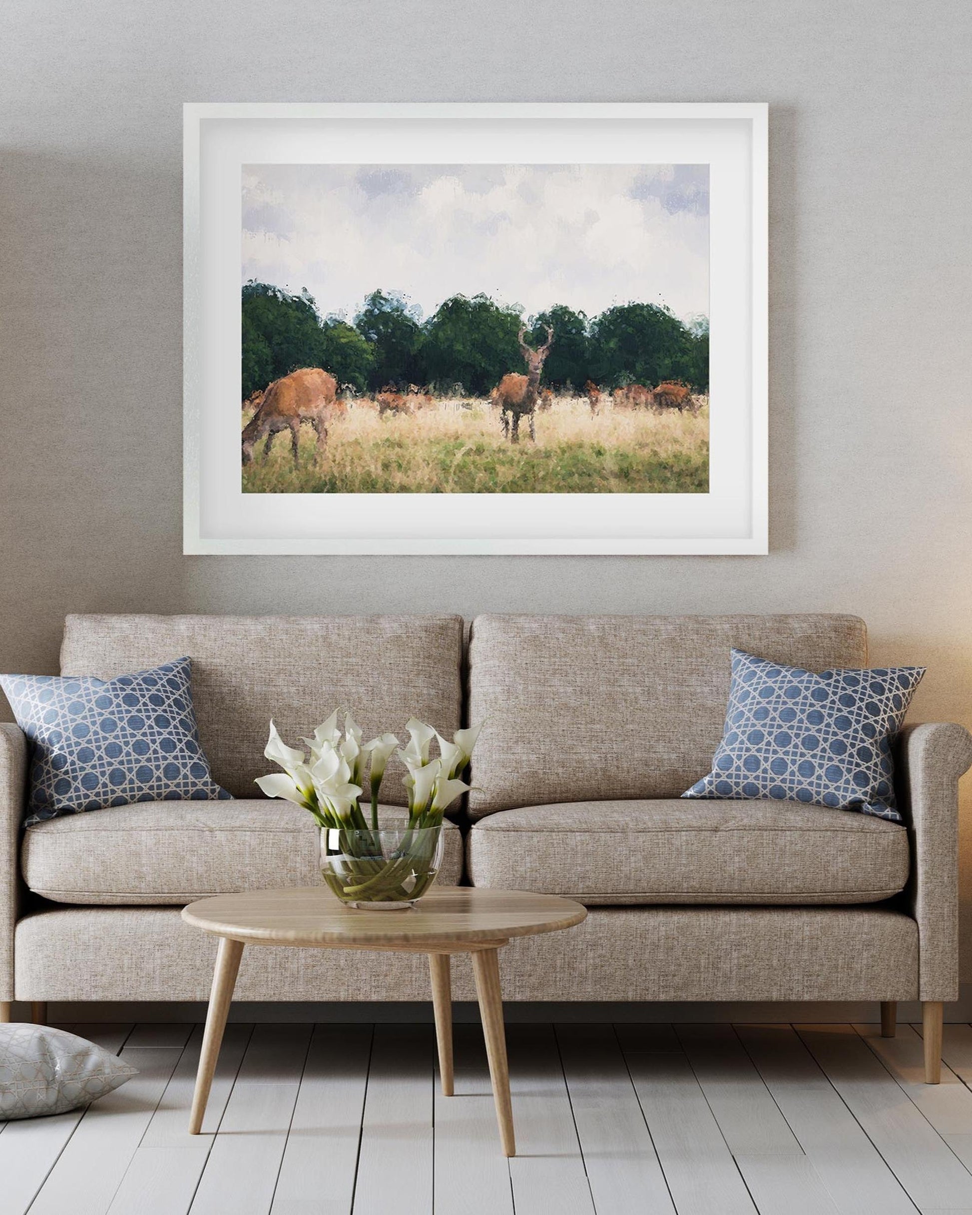 Framed photograph of deer in a field above a beige sofa with decorative pillows.