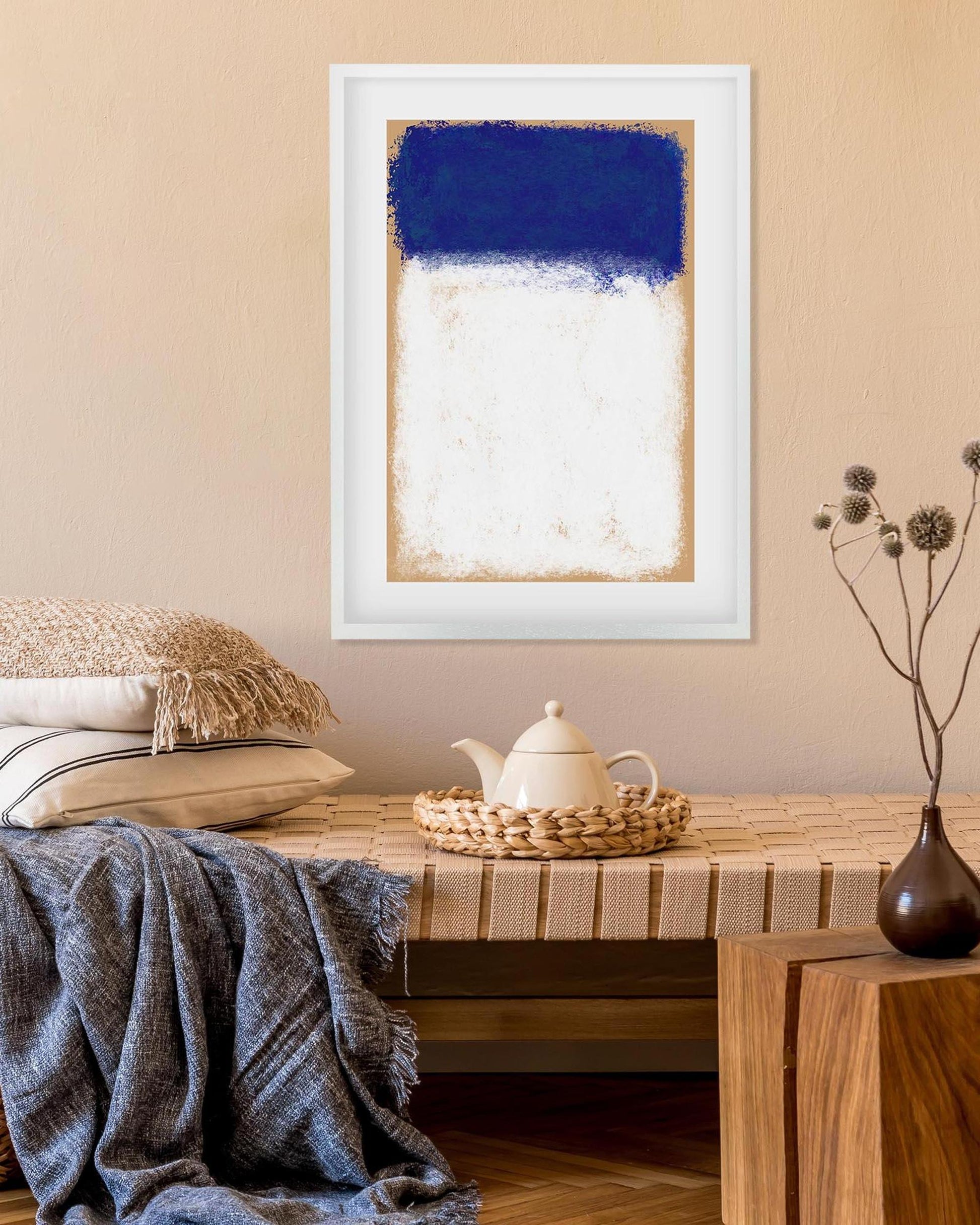 Framed abstract art with blue and white on a wall above a wooden table with a teapot and decorative items.