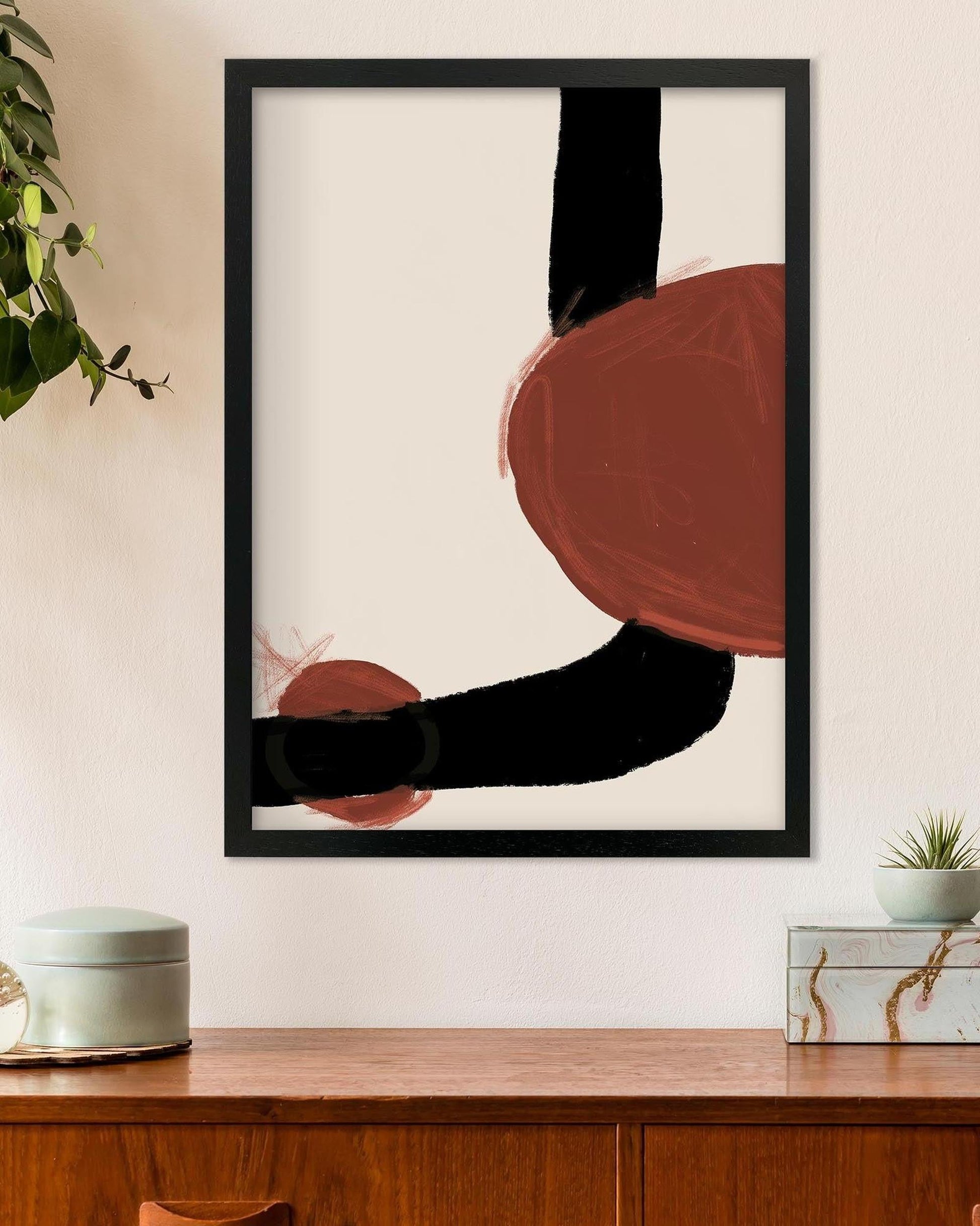 Abstract art print with black and red shapes on a white wall above a wooden shelf.