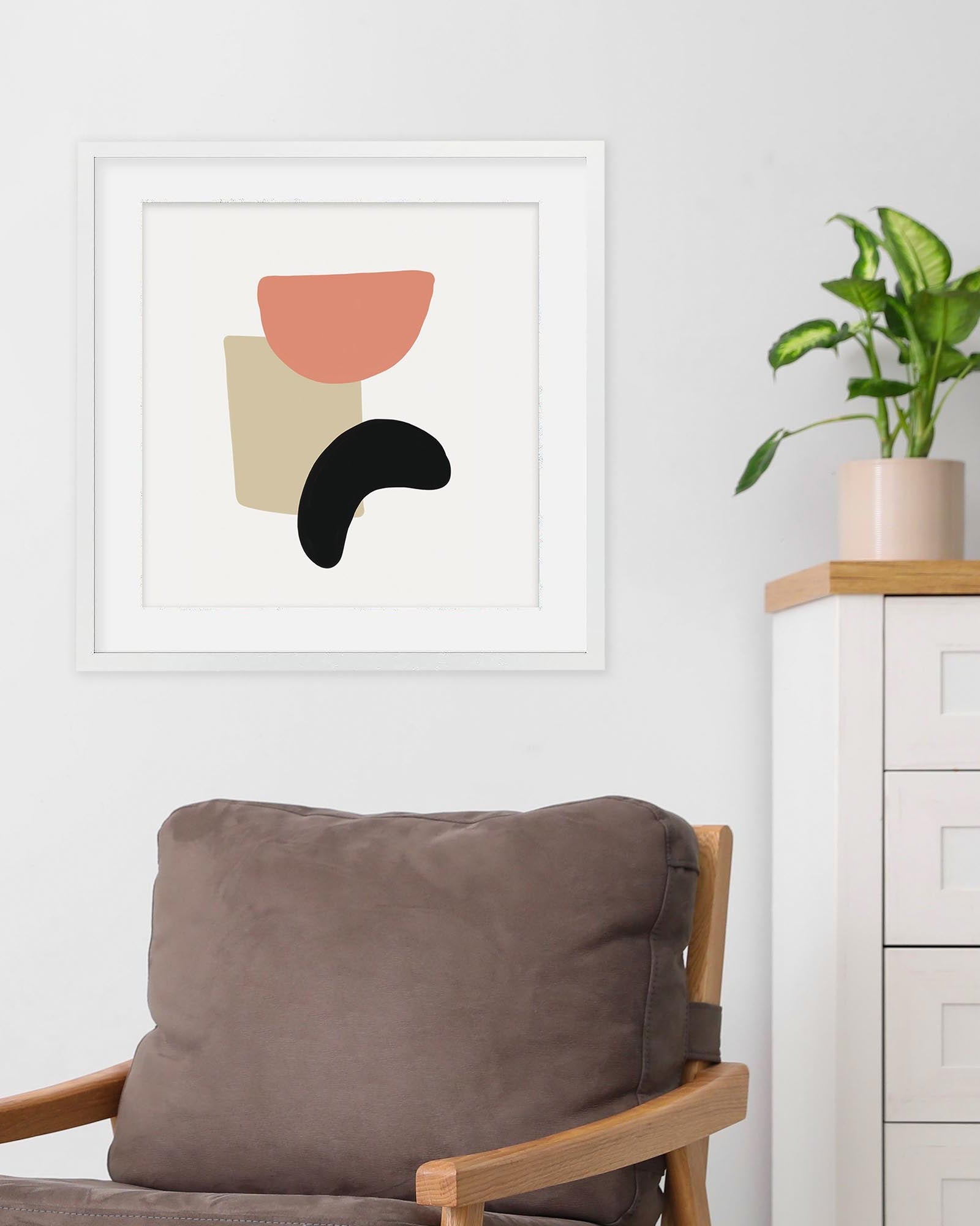 Framed abstract art print on a wall with a chair and plant in the foreground