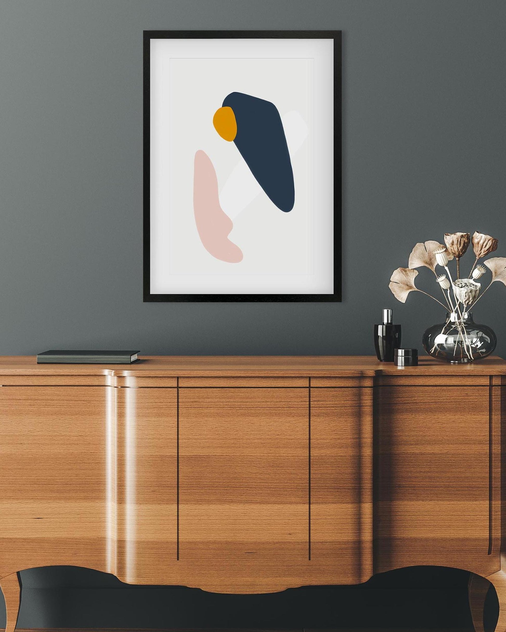 Framed abstract art on a wall above a wooden cabinet with decorative items.