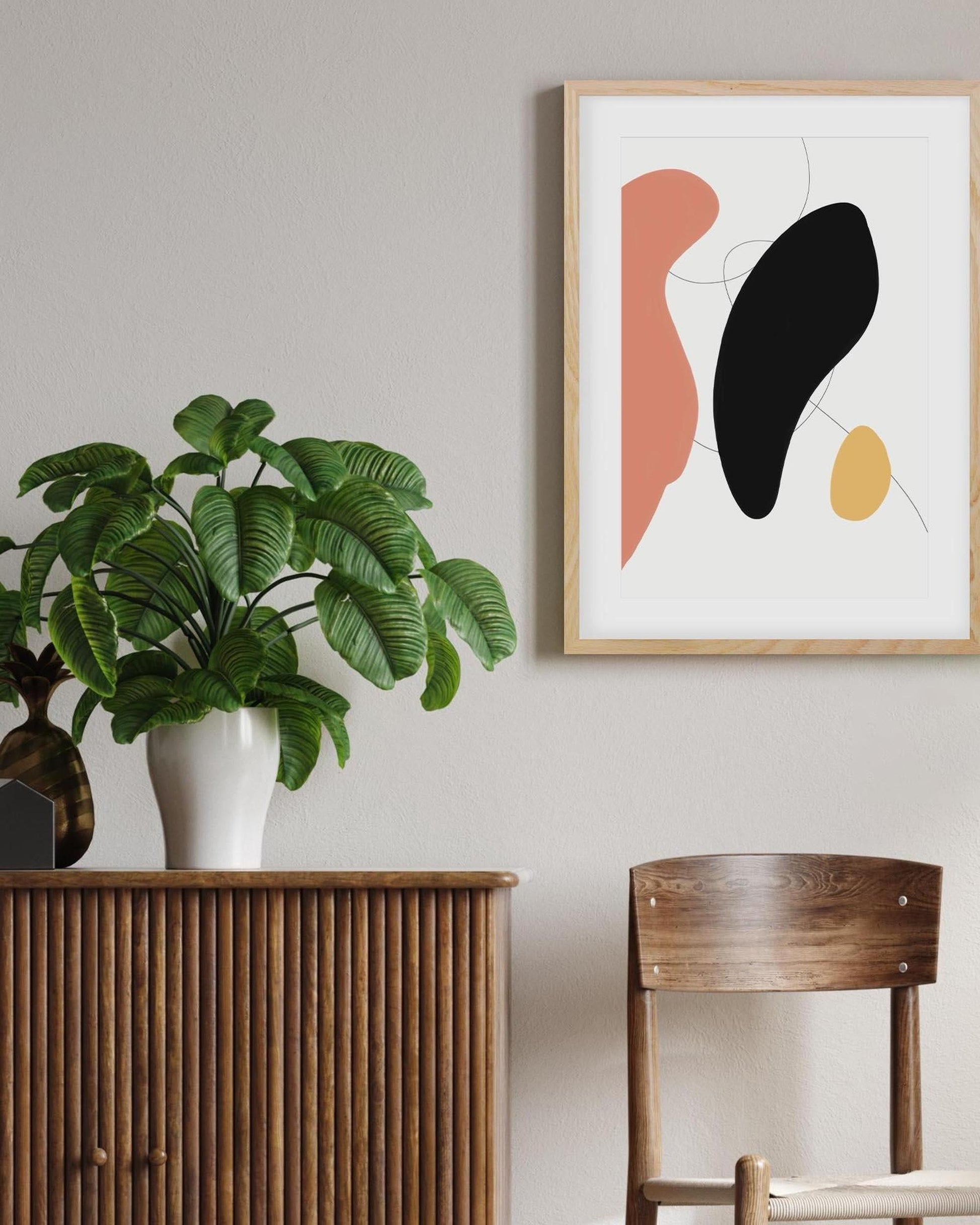 Abstract art print on a wall with a plant and wooden furniture in the foreground.