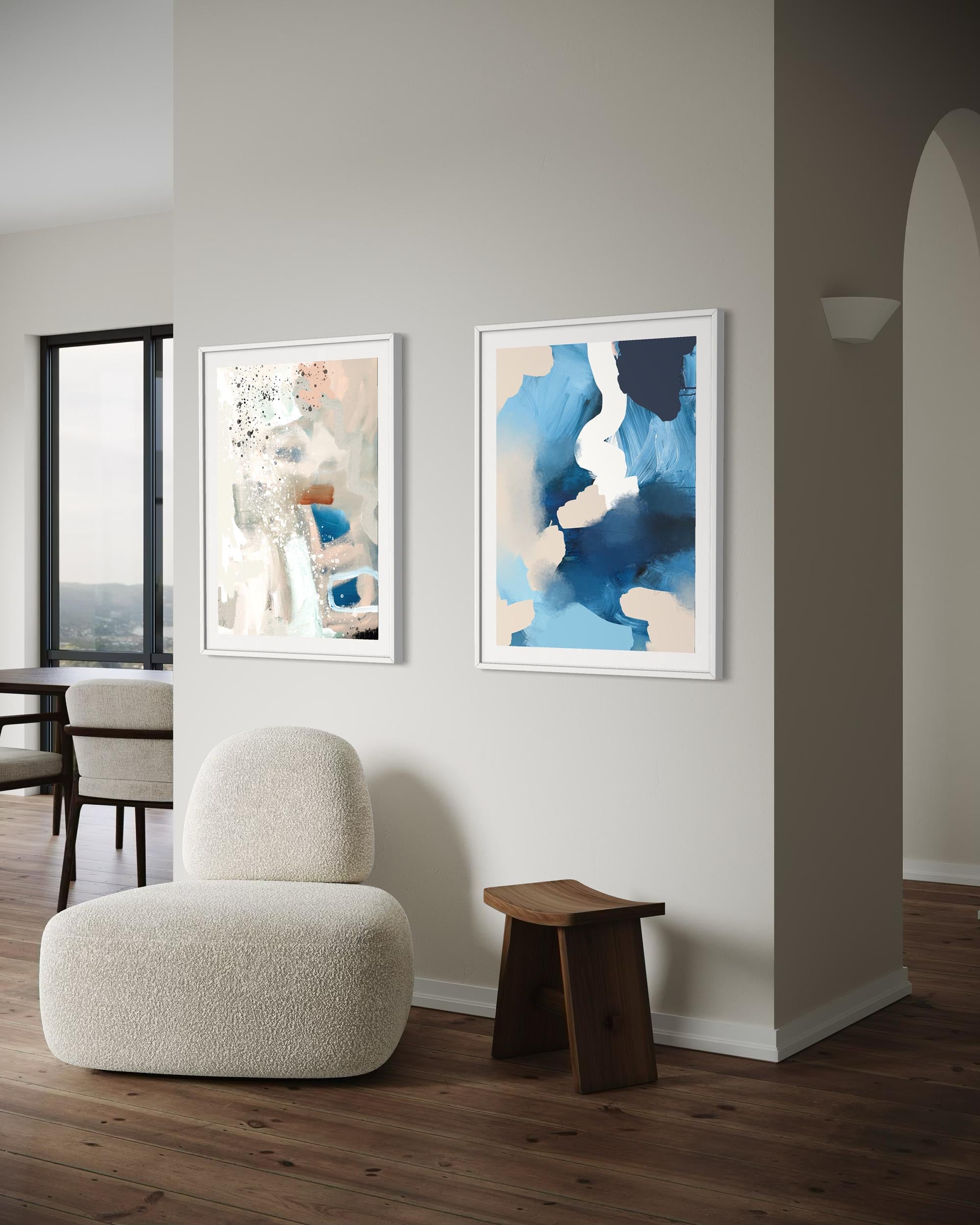 Modern interior with a white armchair, wooden stool, and two framed artworks on a wall.