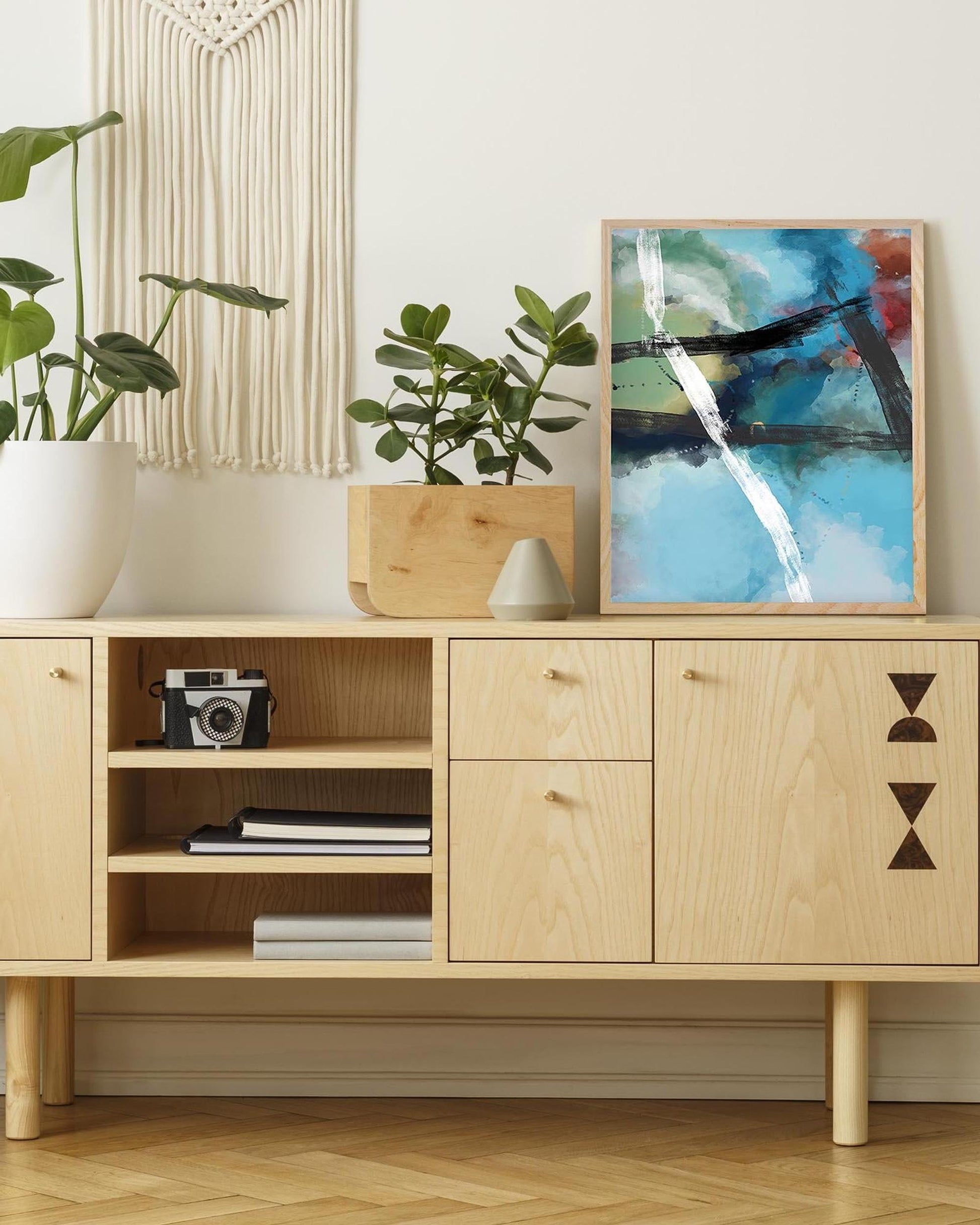 Wooden sideboard with decorative items including a plant, camera, and abstract painting.