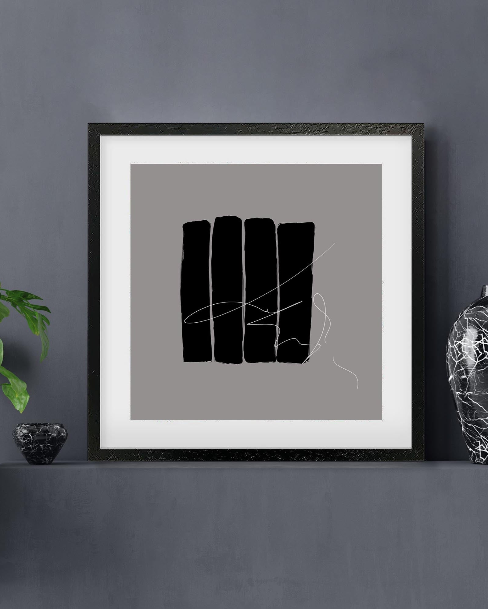 Framed abstract art print with black shapes on a gray background, displayed on a dark wall.