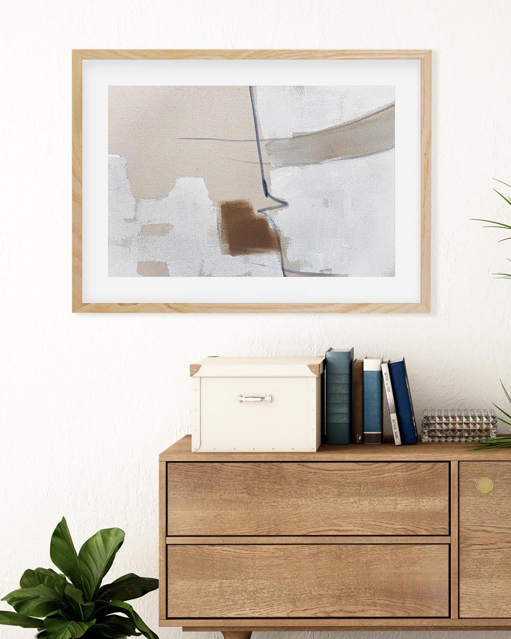 Framed abstract art above a wooden dresser with books and decorative items.