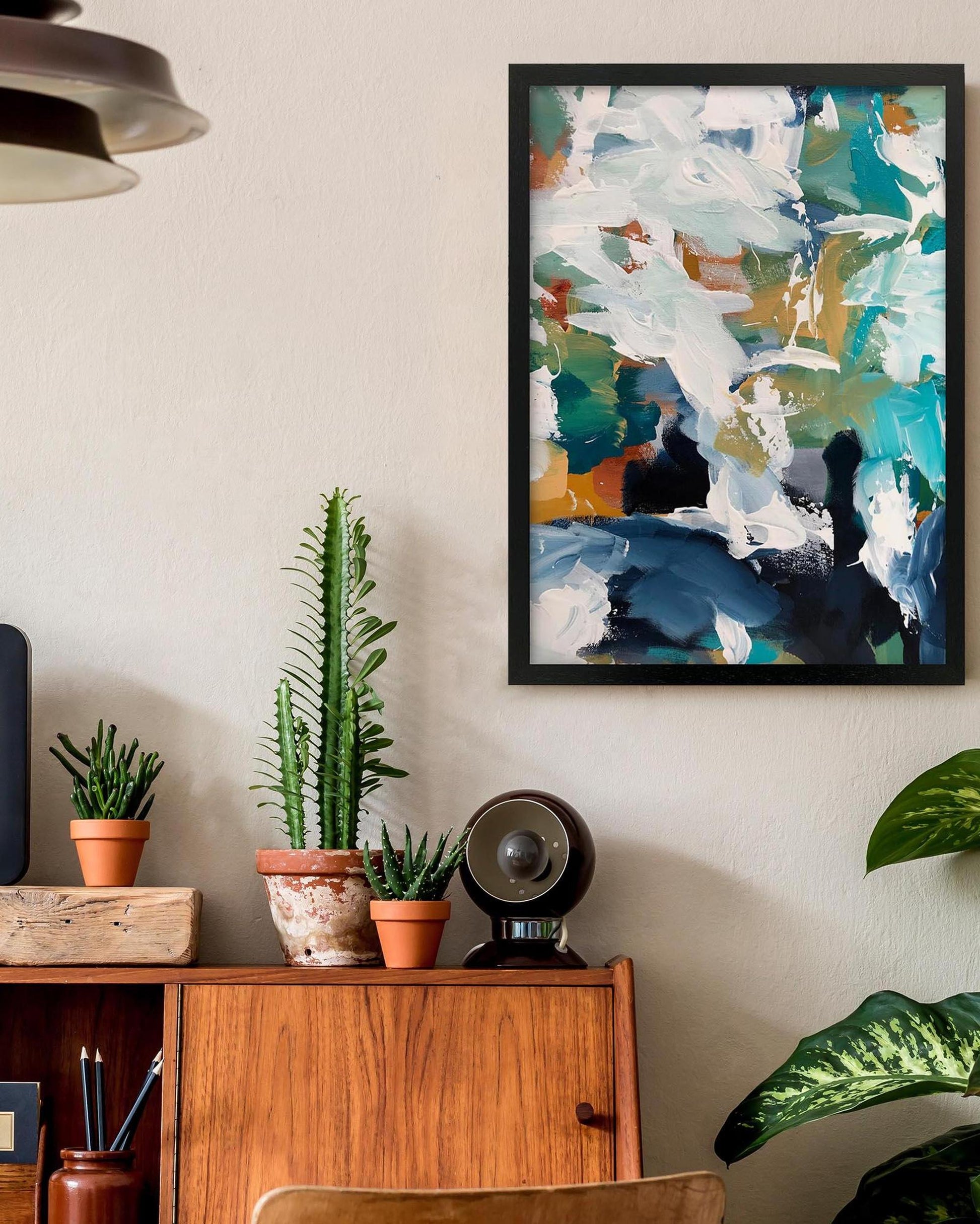 Abstract art print on a wall above a wooden cabinet with plants.