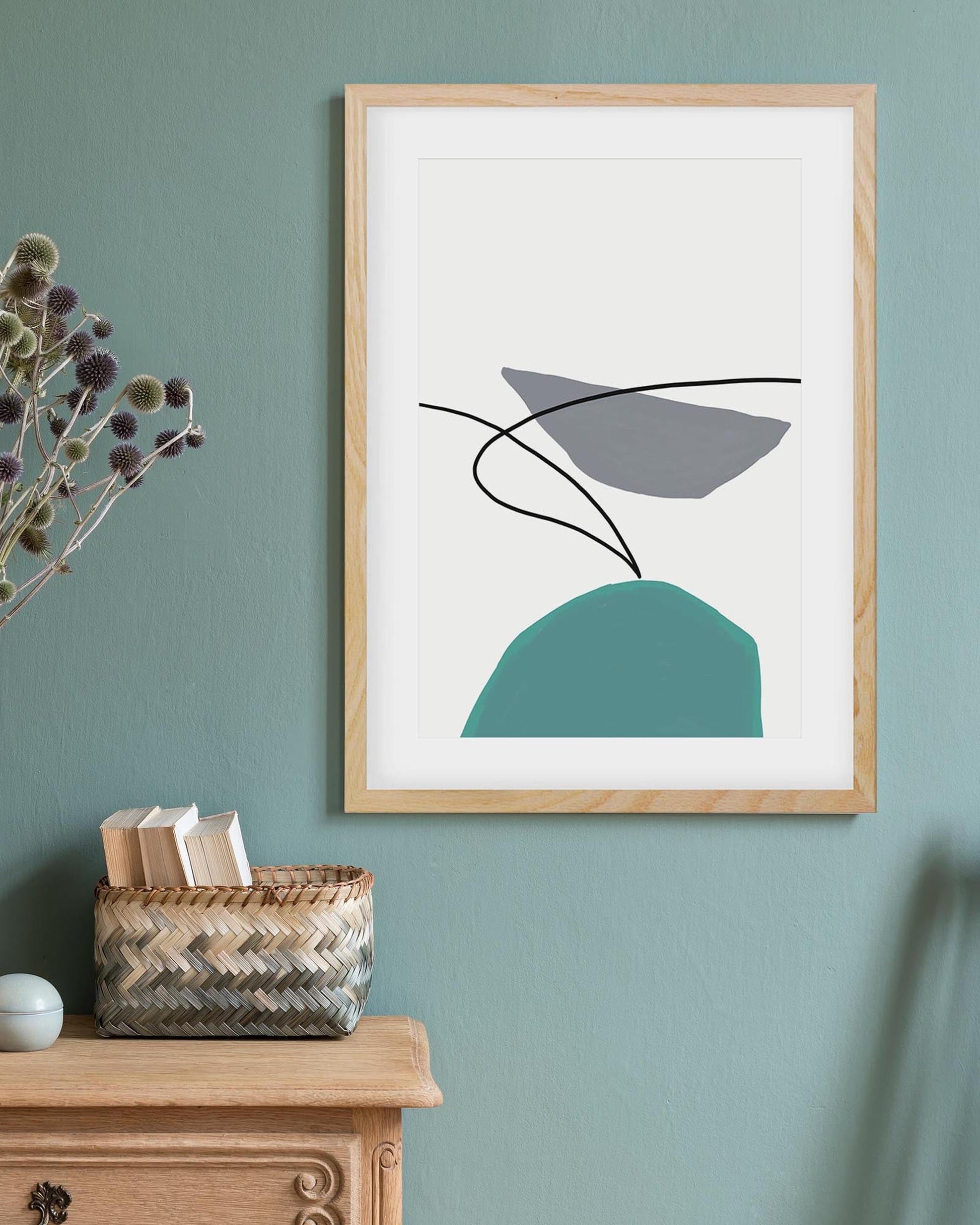 Framed abstract art print on a wall with a wooden cabinet and basket below.