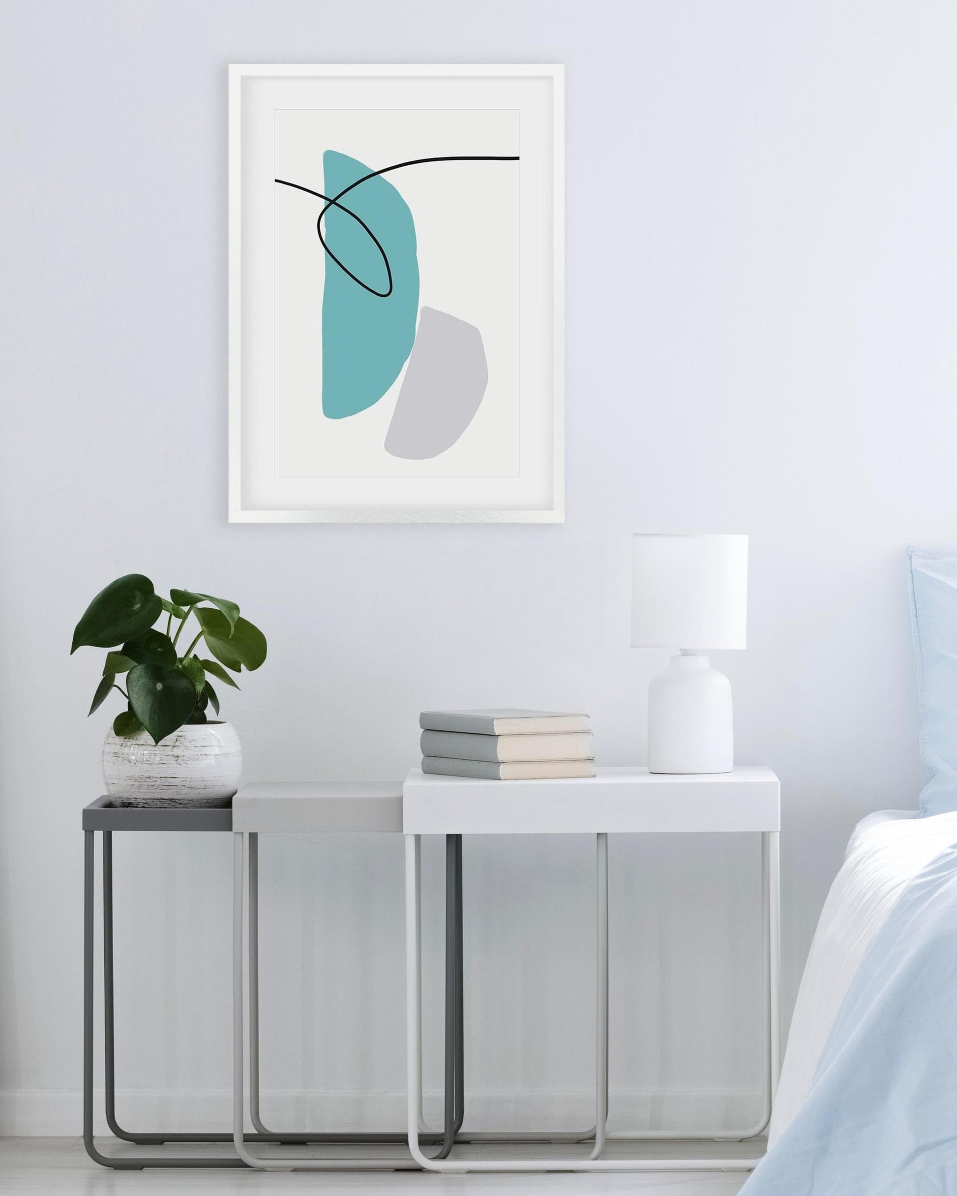 Abstract art print on a wall above a side table with a plant and books.