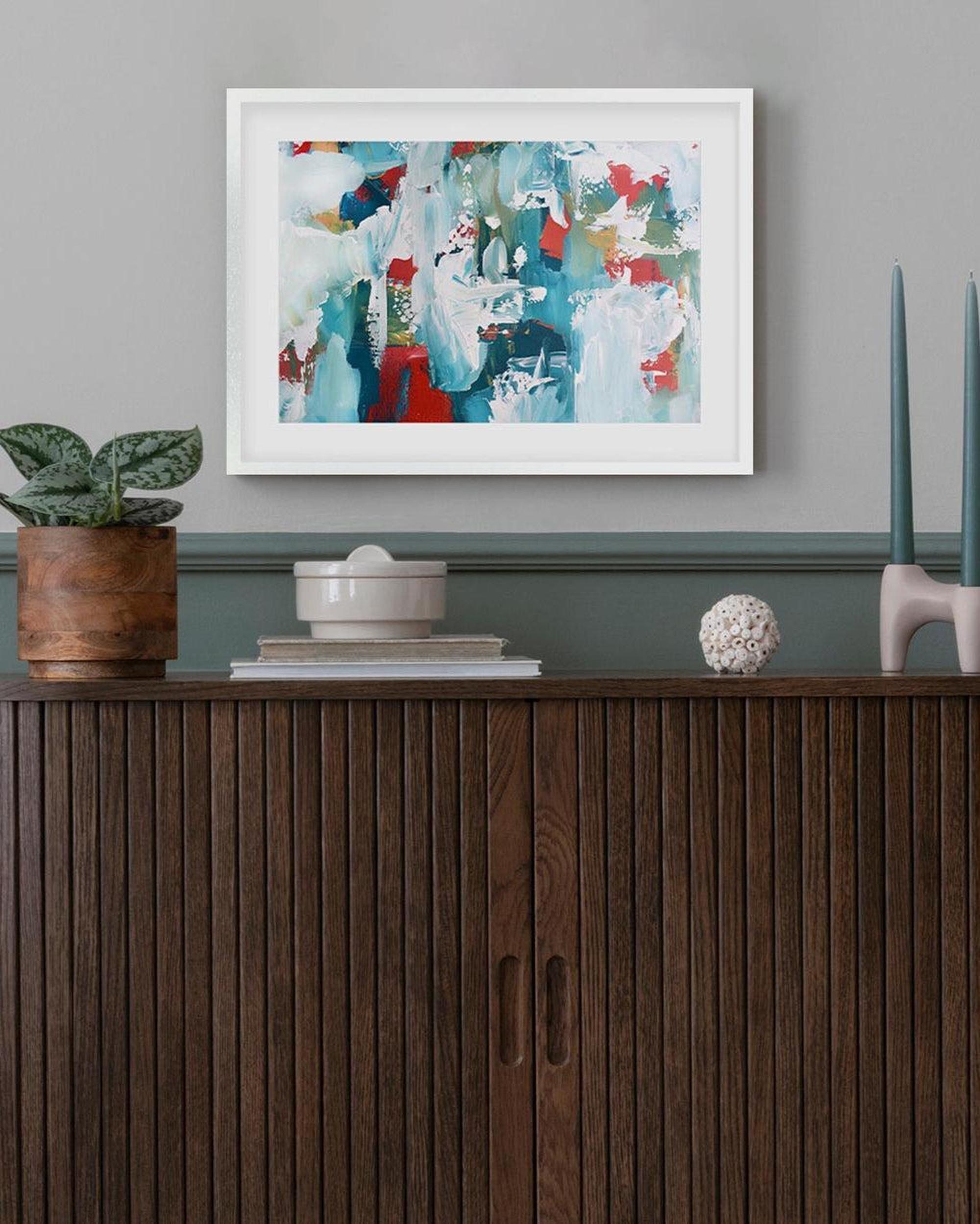 Framed abstract art above a wooden cabinet with decorative items.