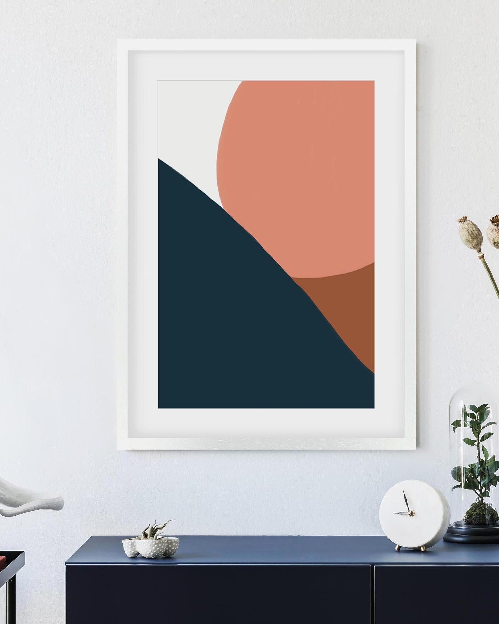 Framed abstract art print with geometric shapes on a wall above a console table.