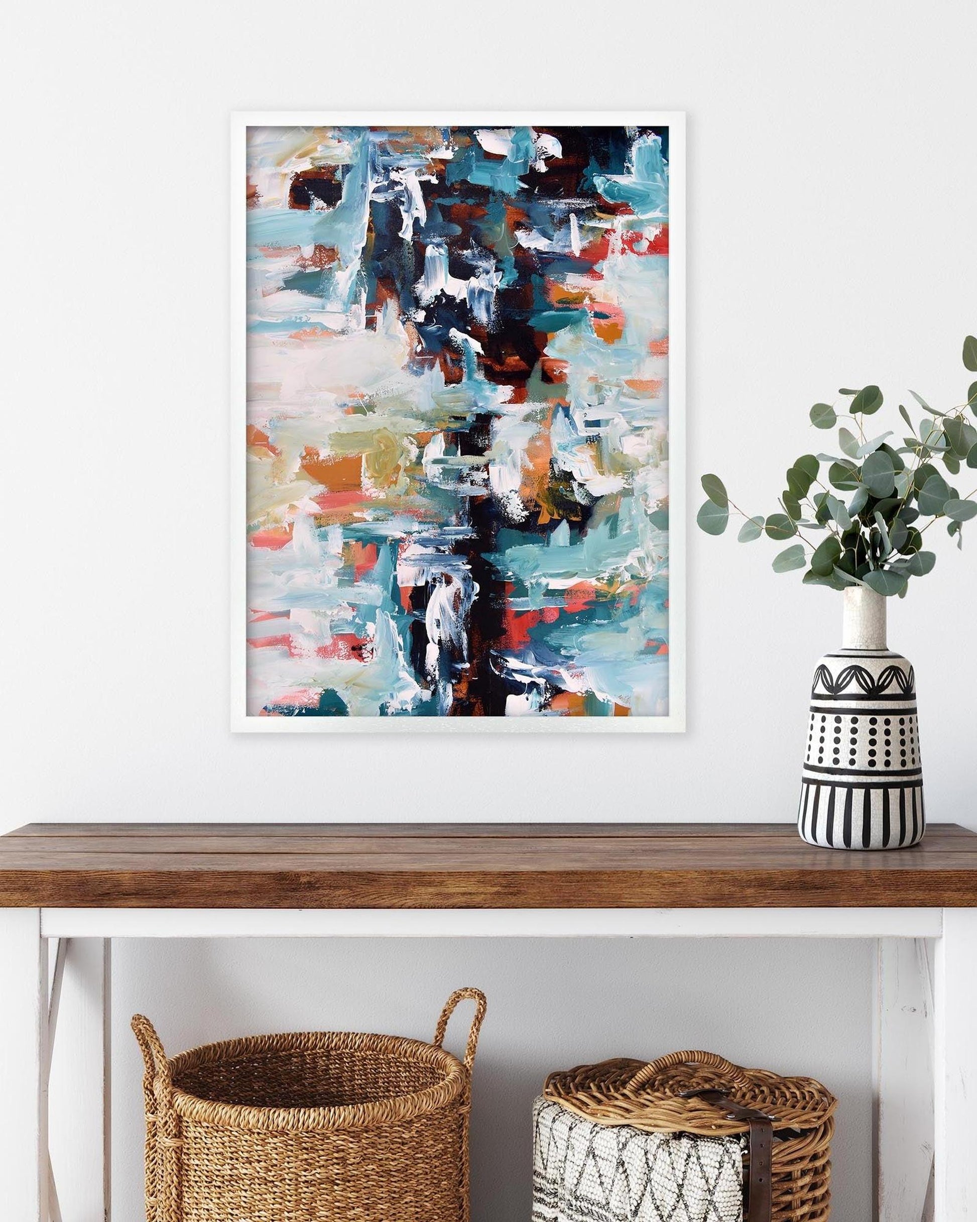 Abstract art print on a wall above a wooden console table with decorative items.