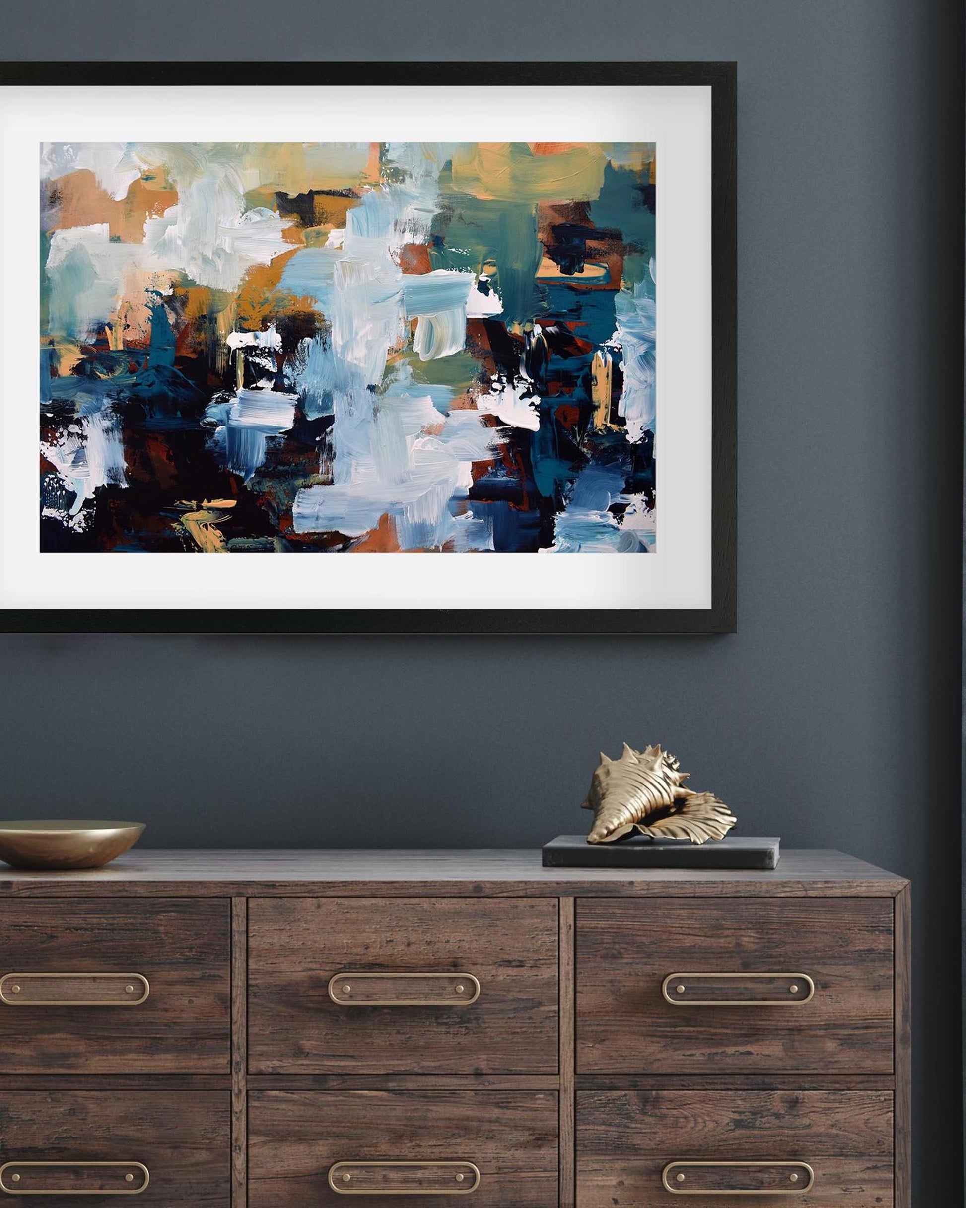 Framed abstract painting on a dark wall above a wooden dresser with decorative items.