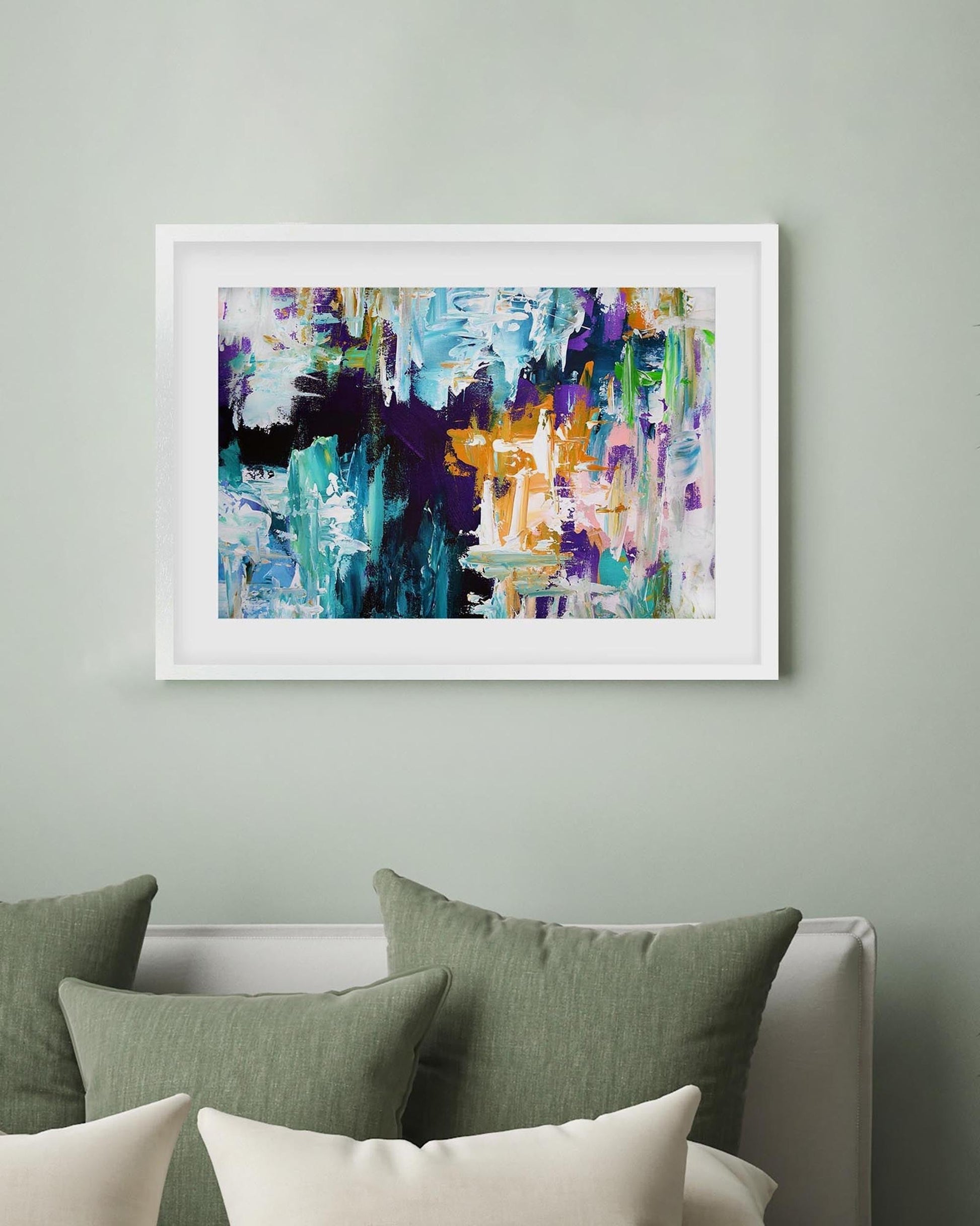 Framed abstract painting on a wall above a bed with green and white pillows.