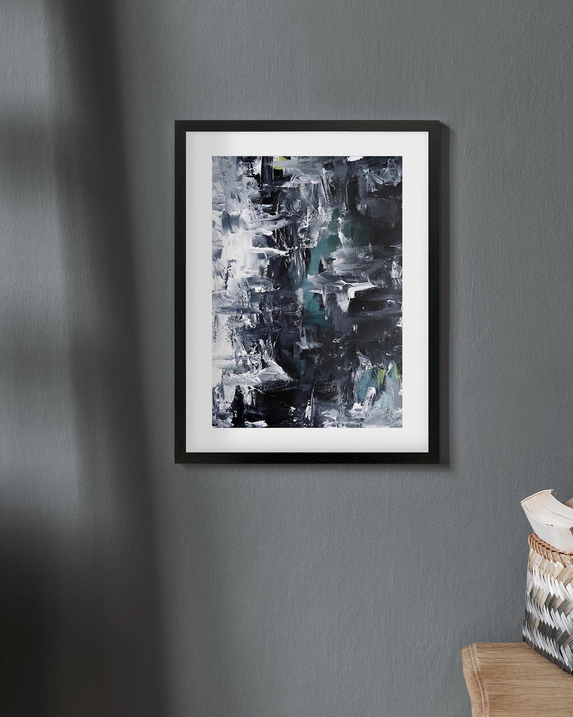 Framed abstract art piece on a gray wall with a basket and towel at the bottom right corner.