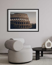 Framed photograph of the Colosseum on a wall above a modern chair and table.